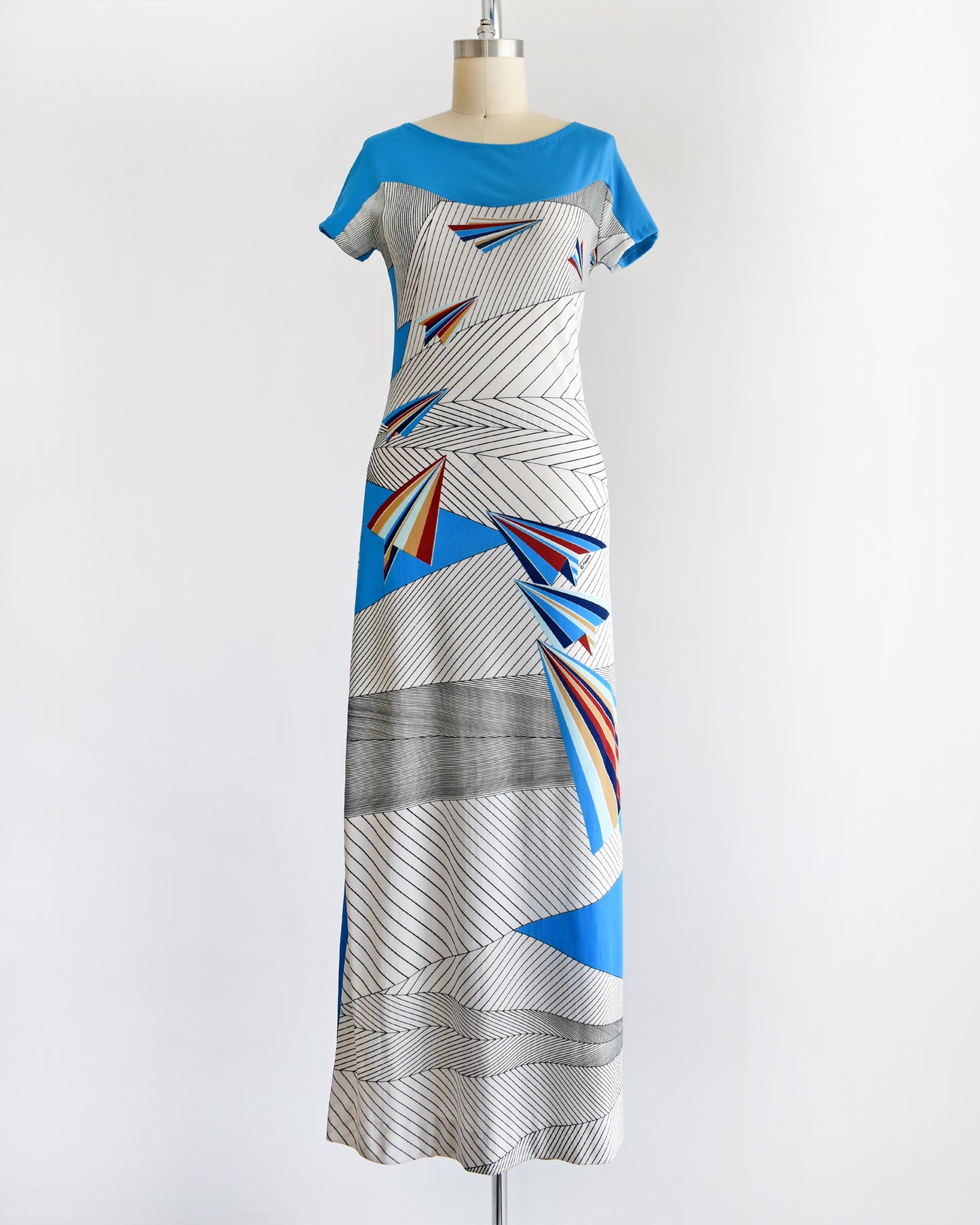 a vintage 1970s dress with geometric patterns and paper planes on a mannequin against a white background