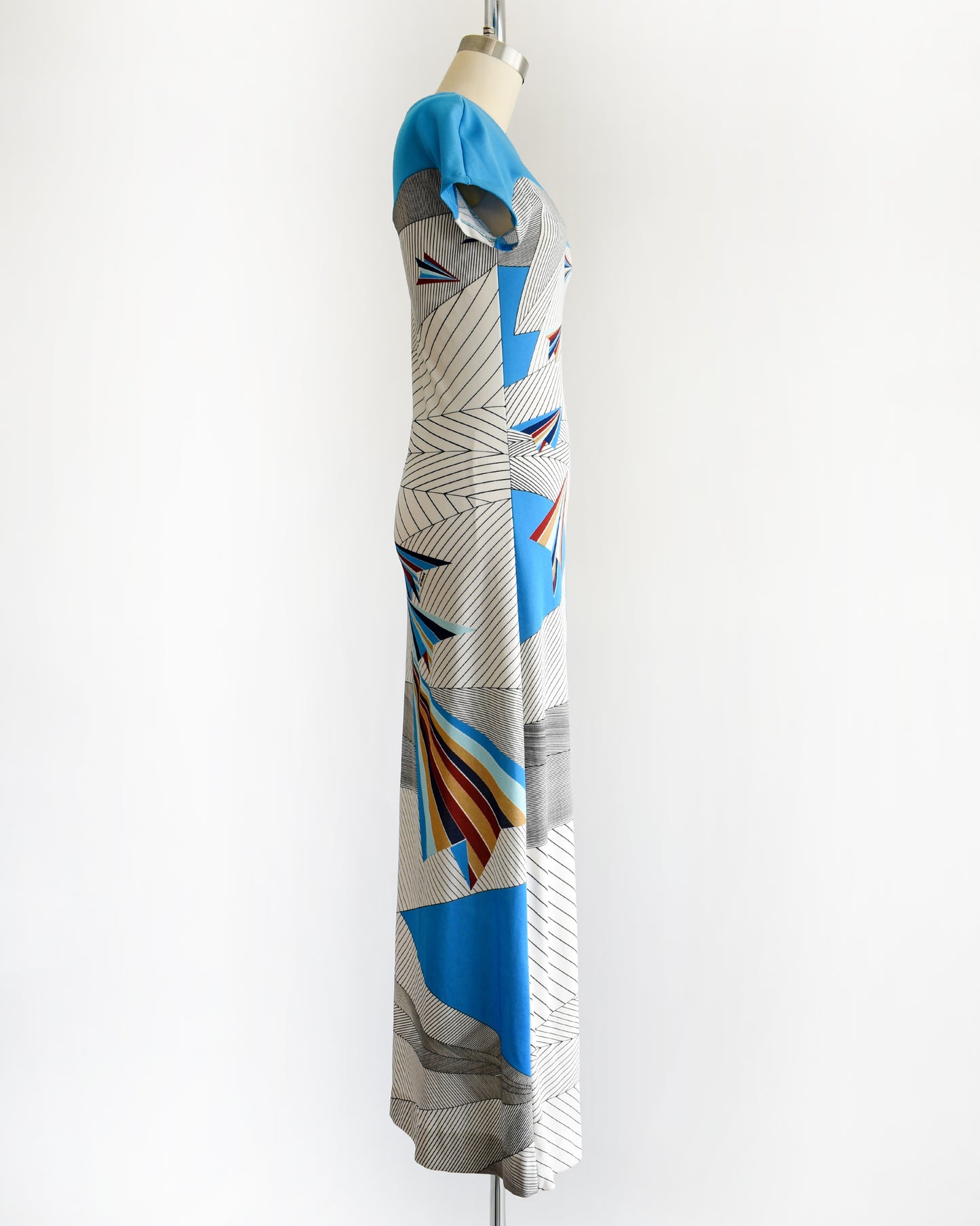 side view of a vintage 1970s dress with geometric patterns and paper planes on a mannequin against a white background