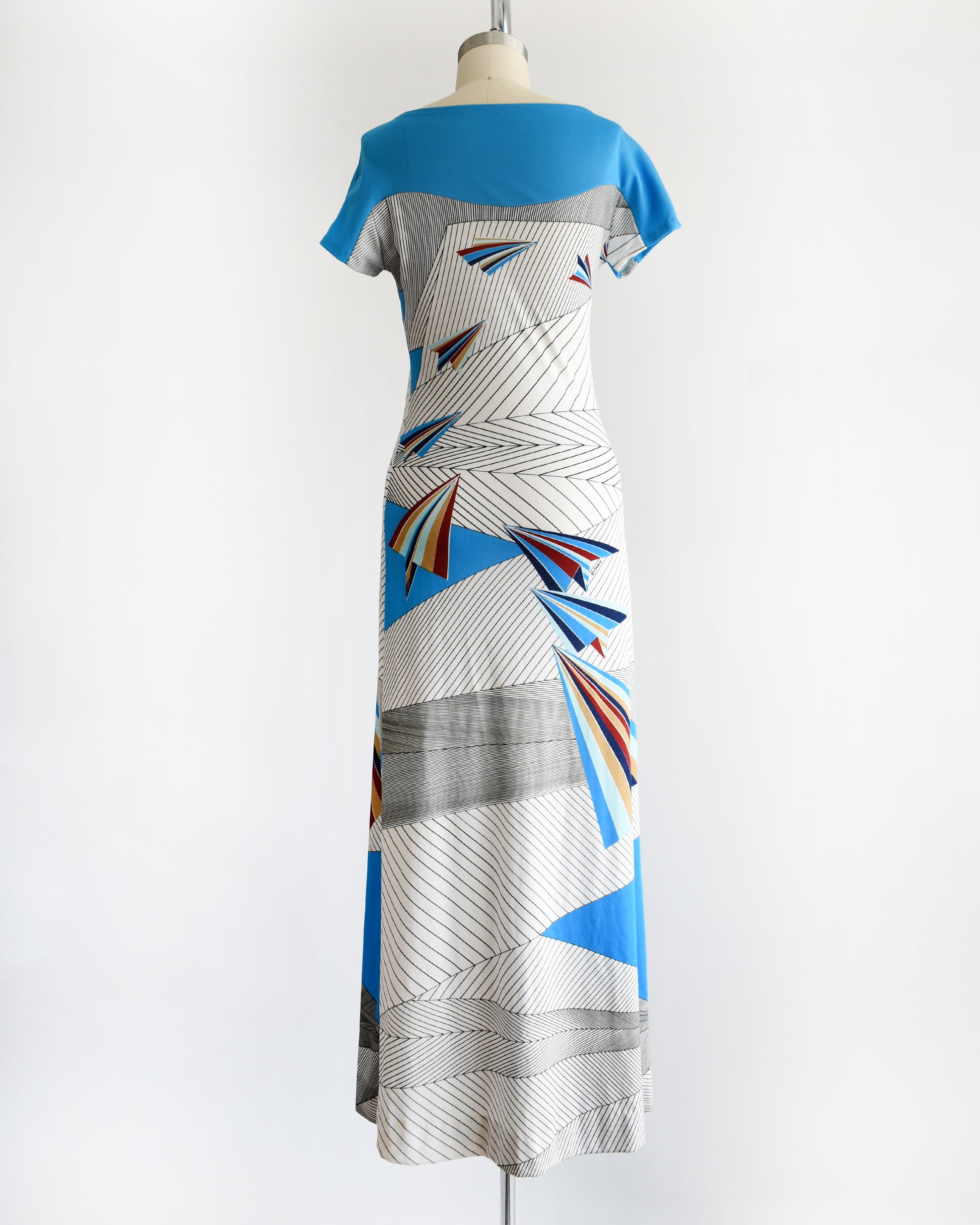 back view of a vintage 1970s dress with geometric patterns and paper planes on a mannequin against a white background