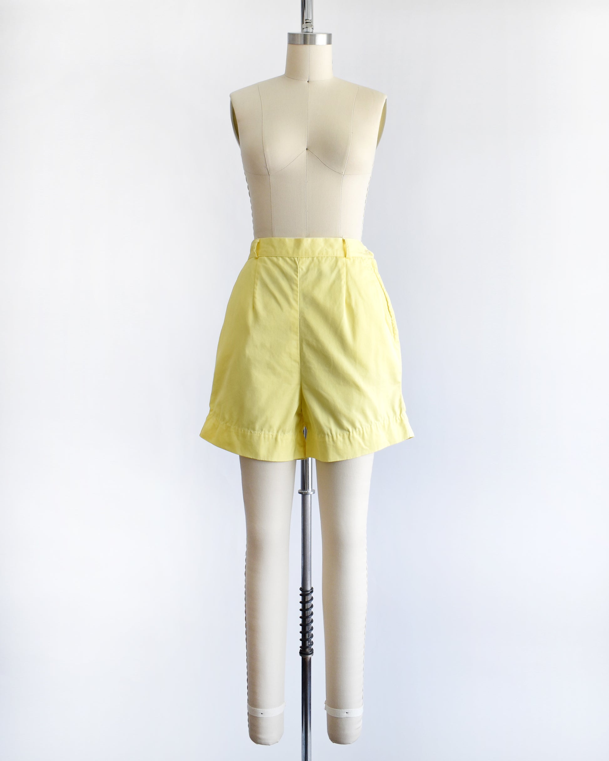 vintage 1960s yellow high-waisted shorts displayed on a mannequin against a white  background.
