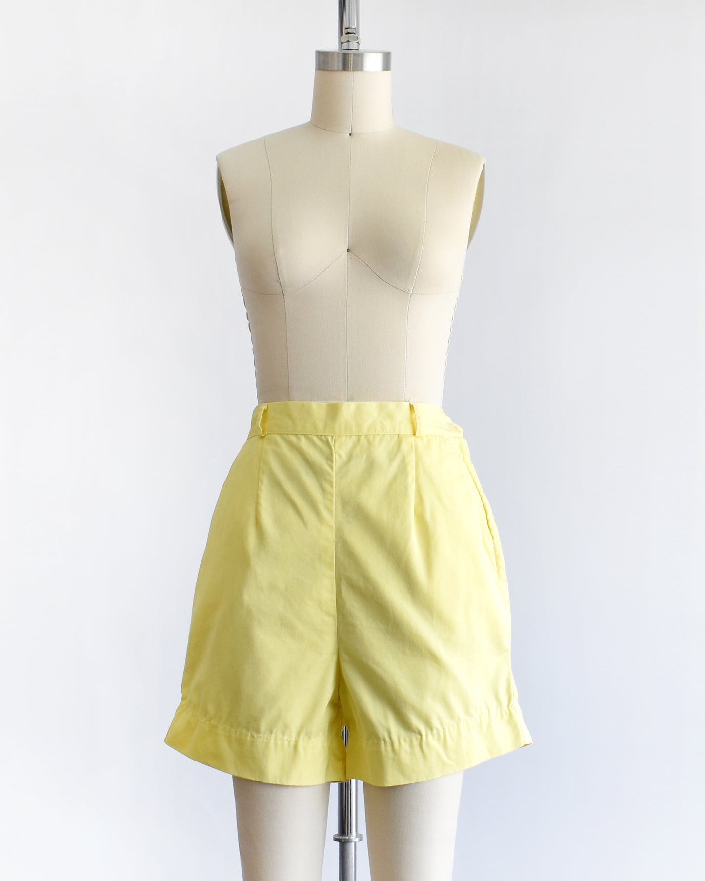 vintage 1960s yellow high-waisted shorts displayed on a mannequin against a white  background.