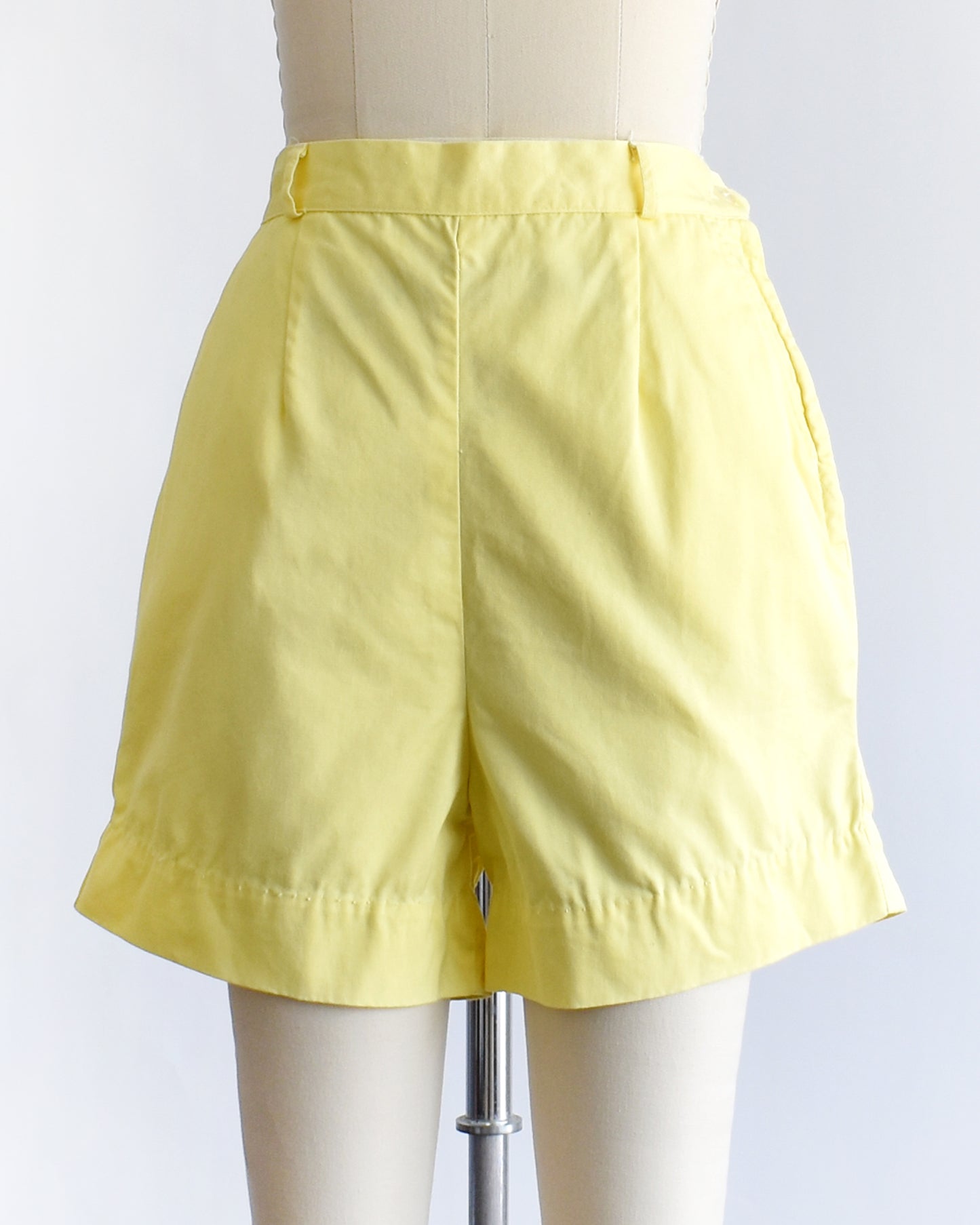 vintage 1960s yellow high-waisted shorts displayed on a mannequin against a white  background.
