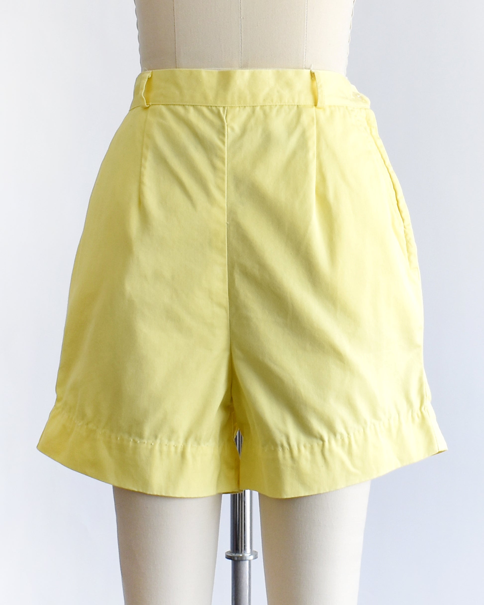 vintage 1960s yellow high-waisted shorts displayed on a mannequin against a white  background.