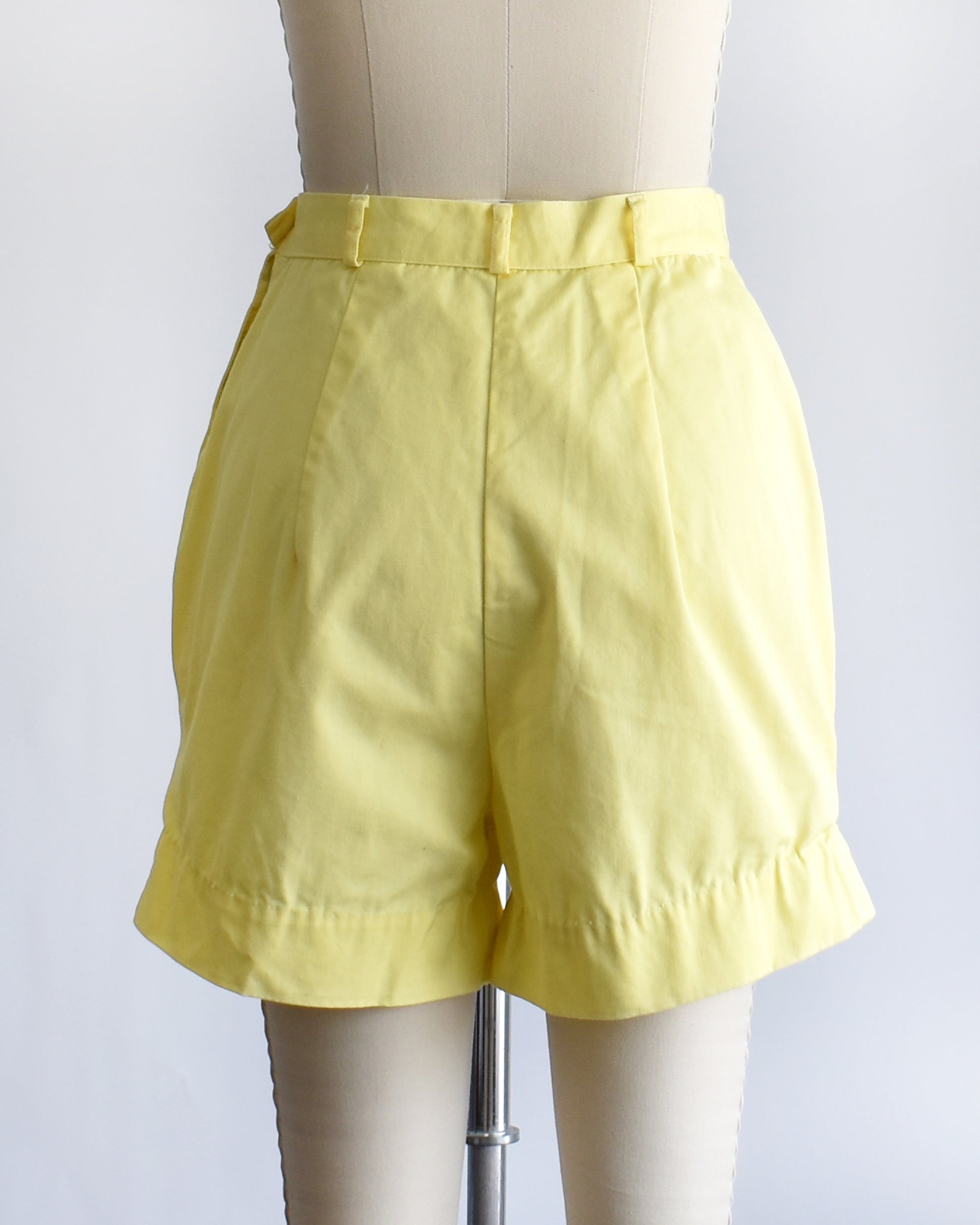back view of vintage 1960s yellow high-waisted shorts displayed on a mannequin against a white  background.