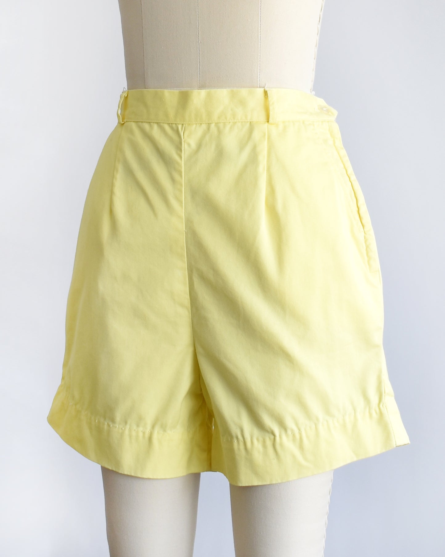 side front view of vintage 1960s yellow high-waisted shorts displayed on a mannequin against a white  background.