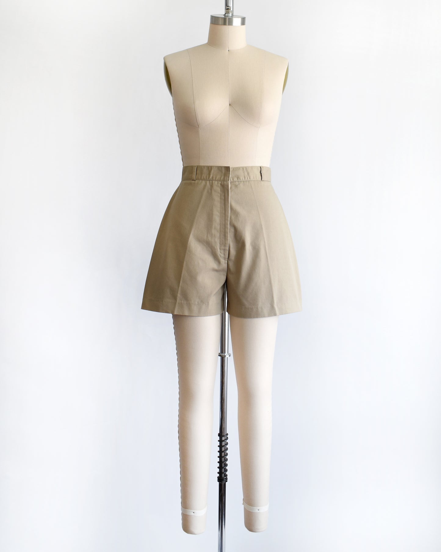 A pair of beige high-waisted shorts displayed on a cream dress form mannequin against a plain white background.