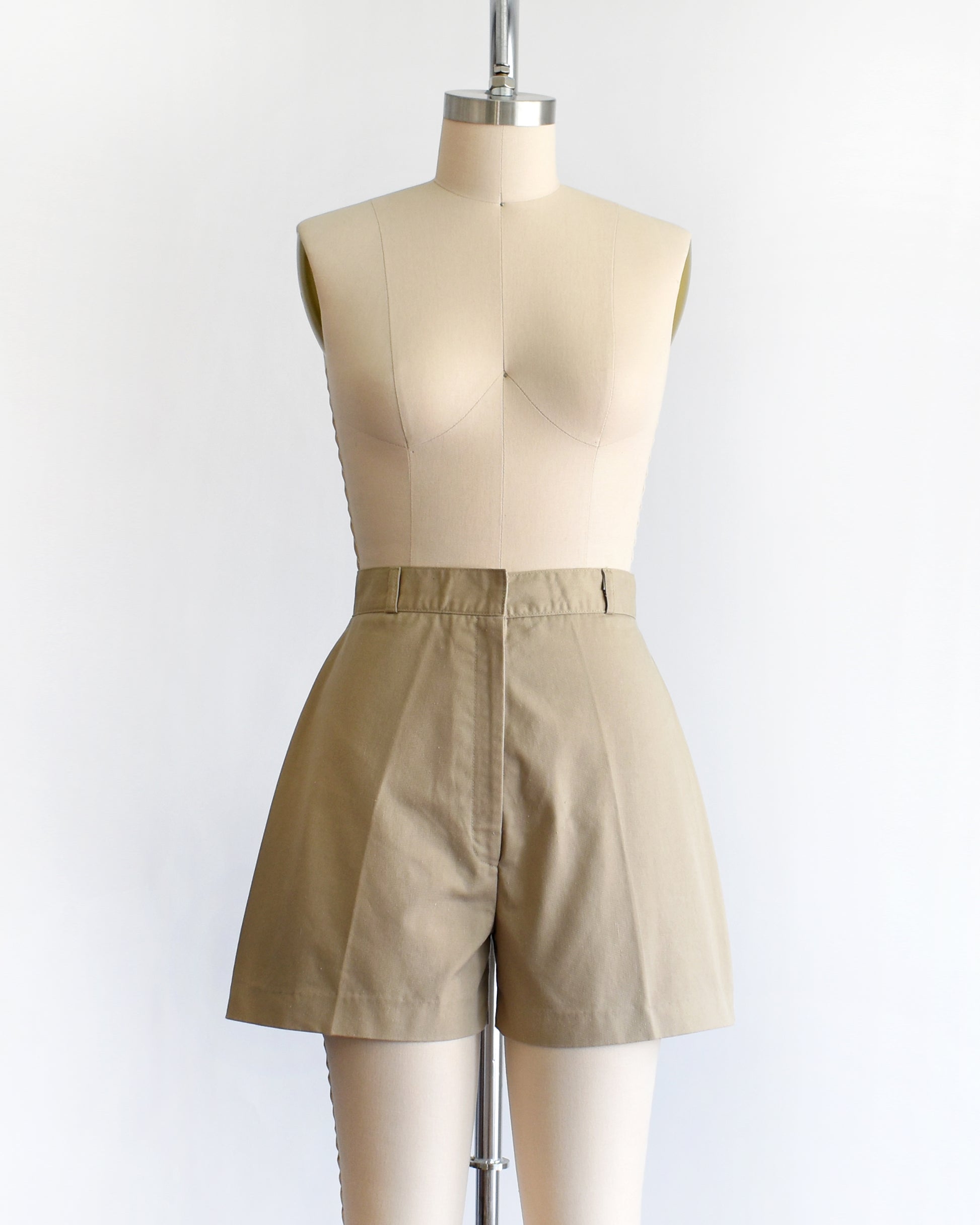 A pair of beige high-waisted shorts displayed on a cream dress form mannequin against a plain white background.