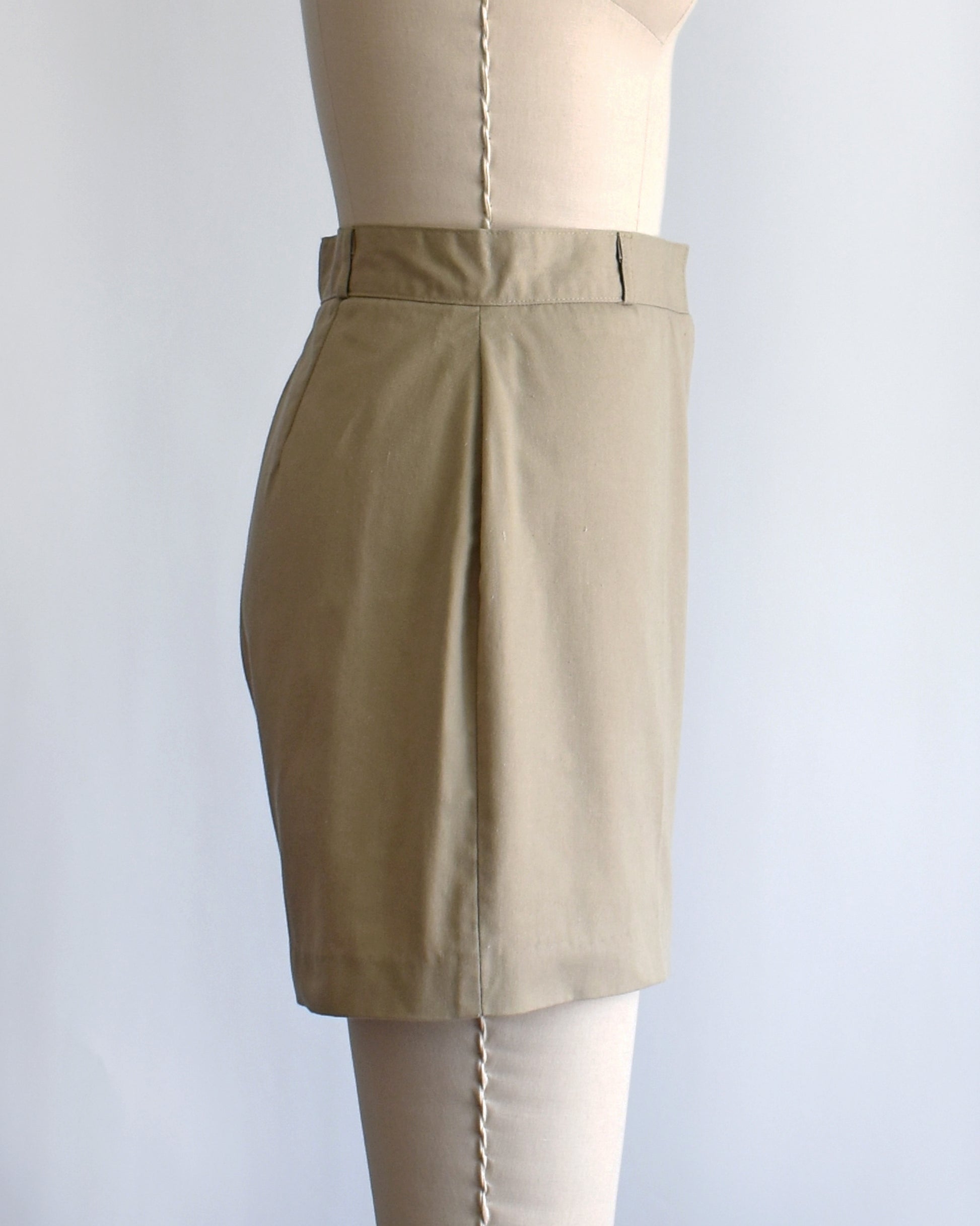 side view of a pair of beige high-waisted shorts displayed on a cream dress form mannequin against a plain white background.