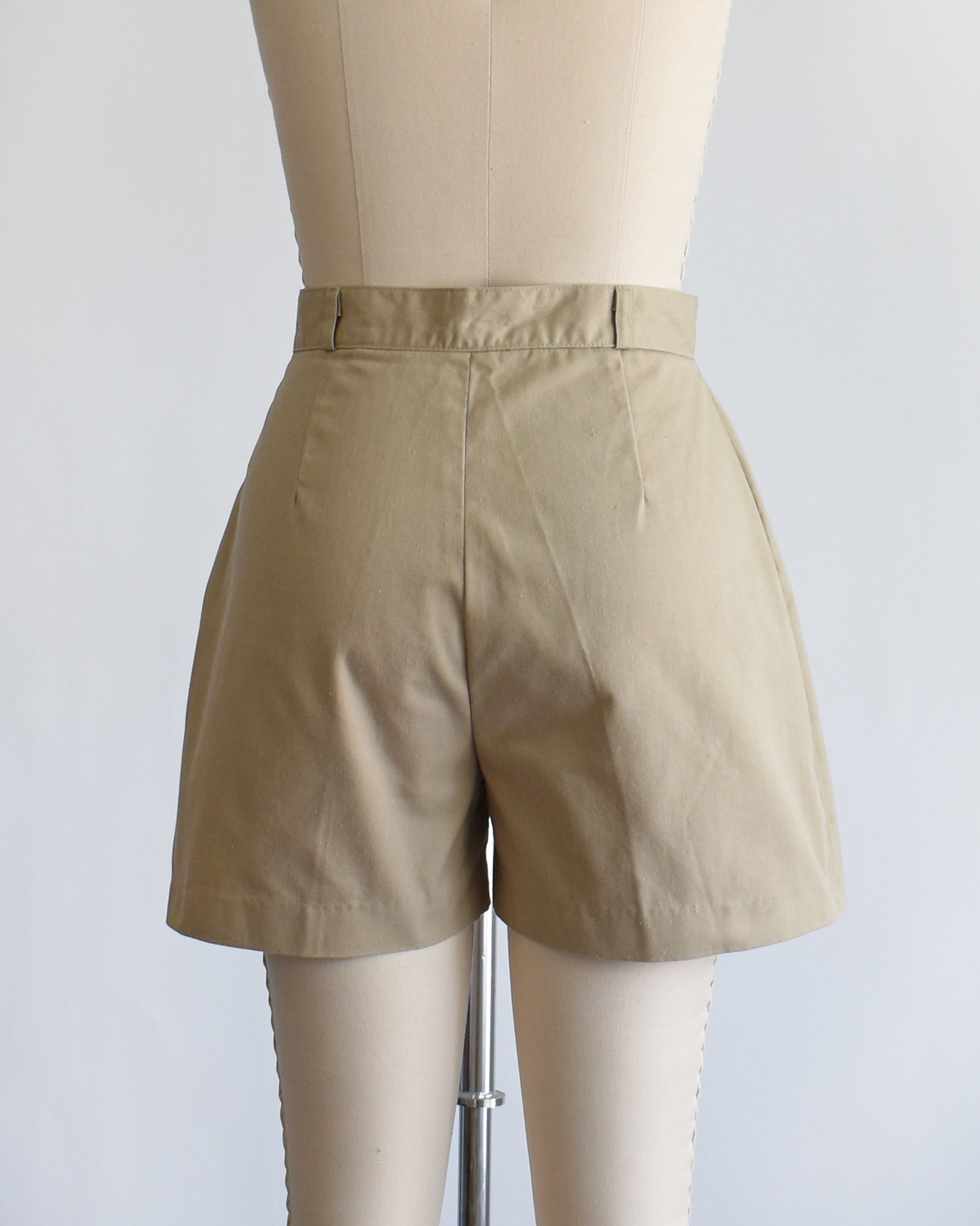 back view of a pair of beige high-waisted shorts displayed on a cream dress form mannequin against a plain white background.