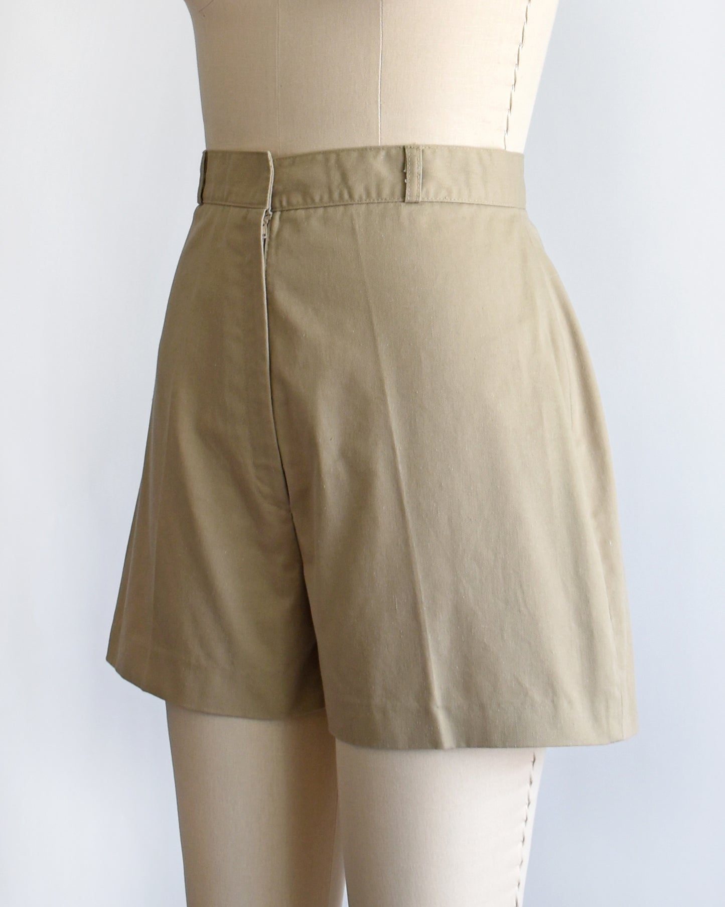 side front view of a pair of beige high-waisted shorts displayed on a cream dress form mannequin against a plain white background.