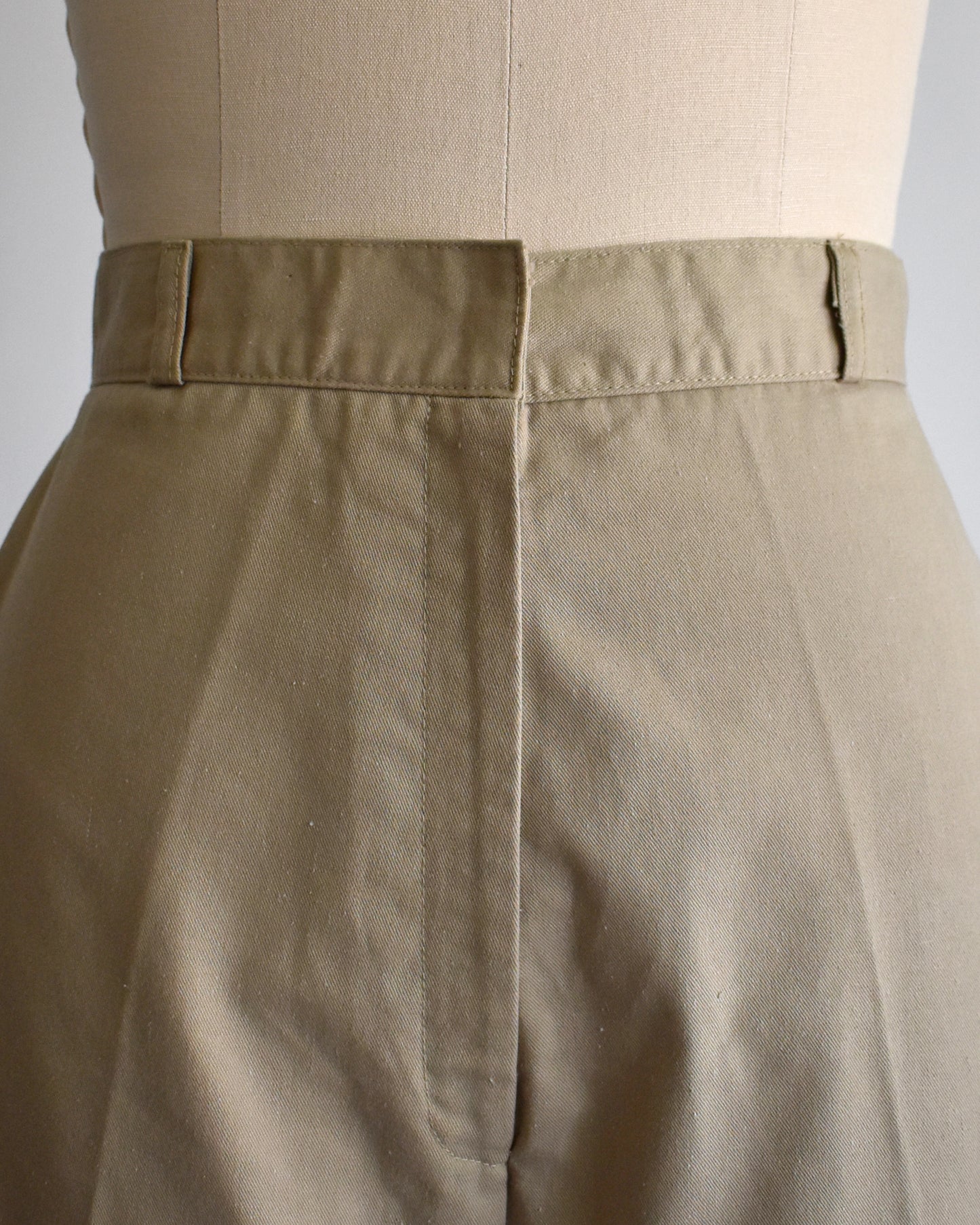 close up of the waistband of a pair of beige high-waisted shorts displayed on a cream dress form mannequin against a plain white background.