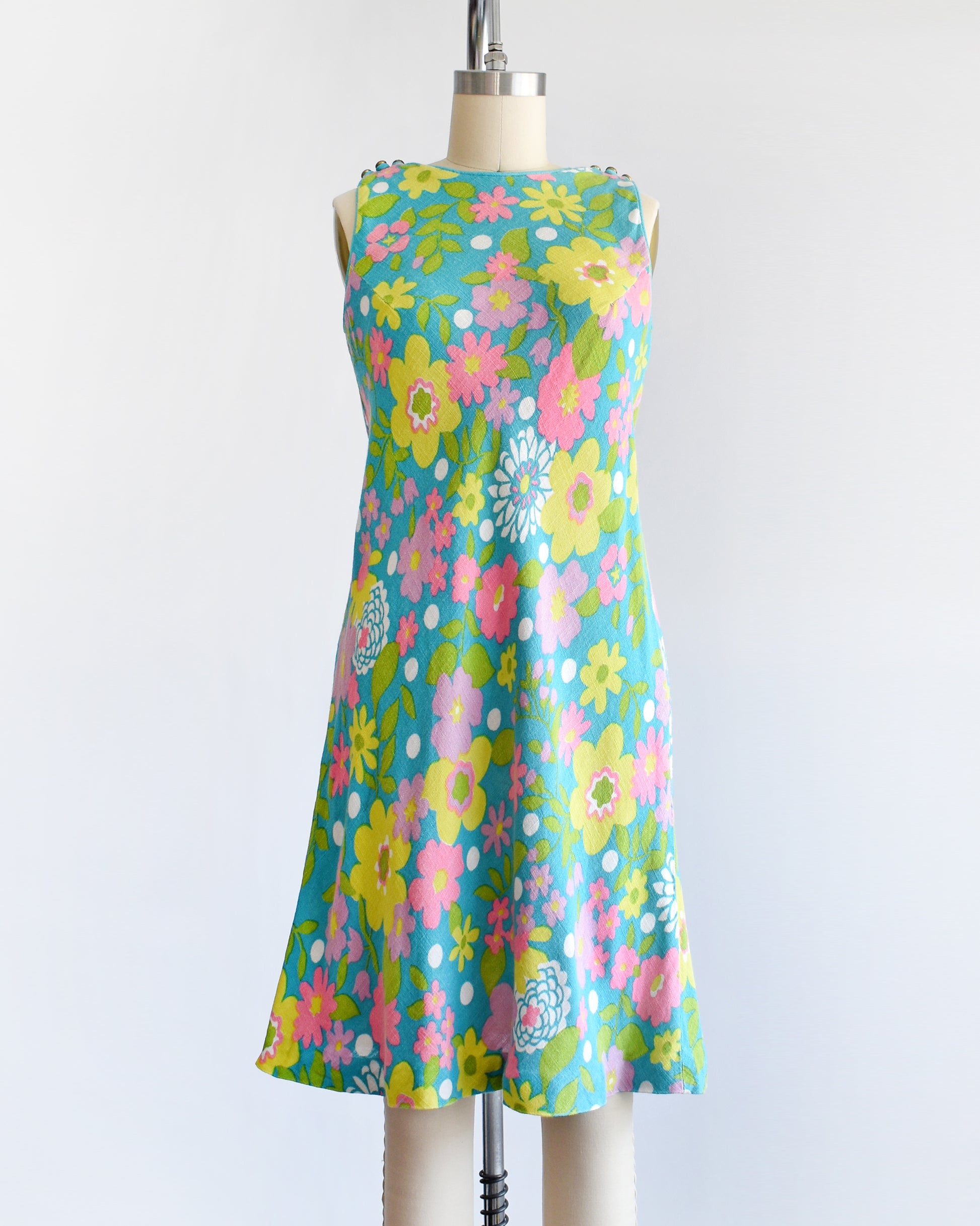 A vintage 1960s blue dress that has a flower power print in pinks, yellows, greens, and white. The dress is on a dress form.