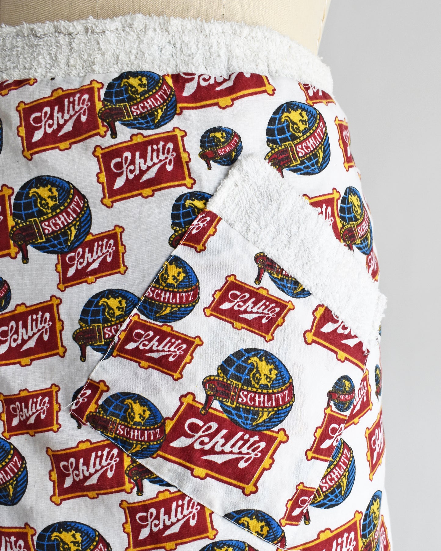 close up of the pocket on a vintage Schlitz terry cloth wrap towel skirt on a dress form against a white background