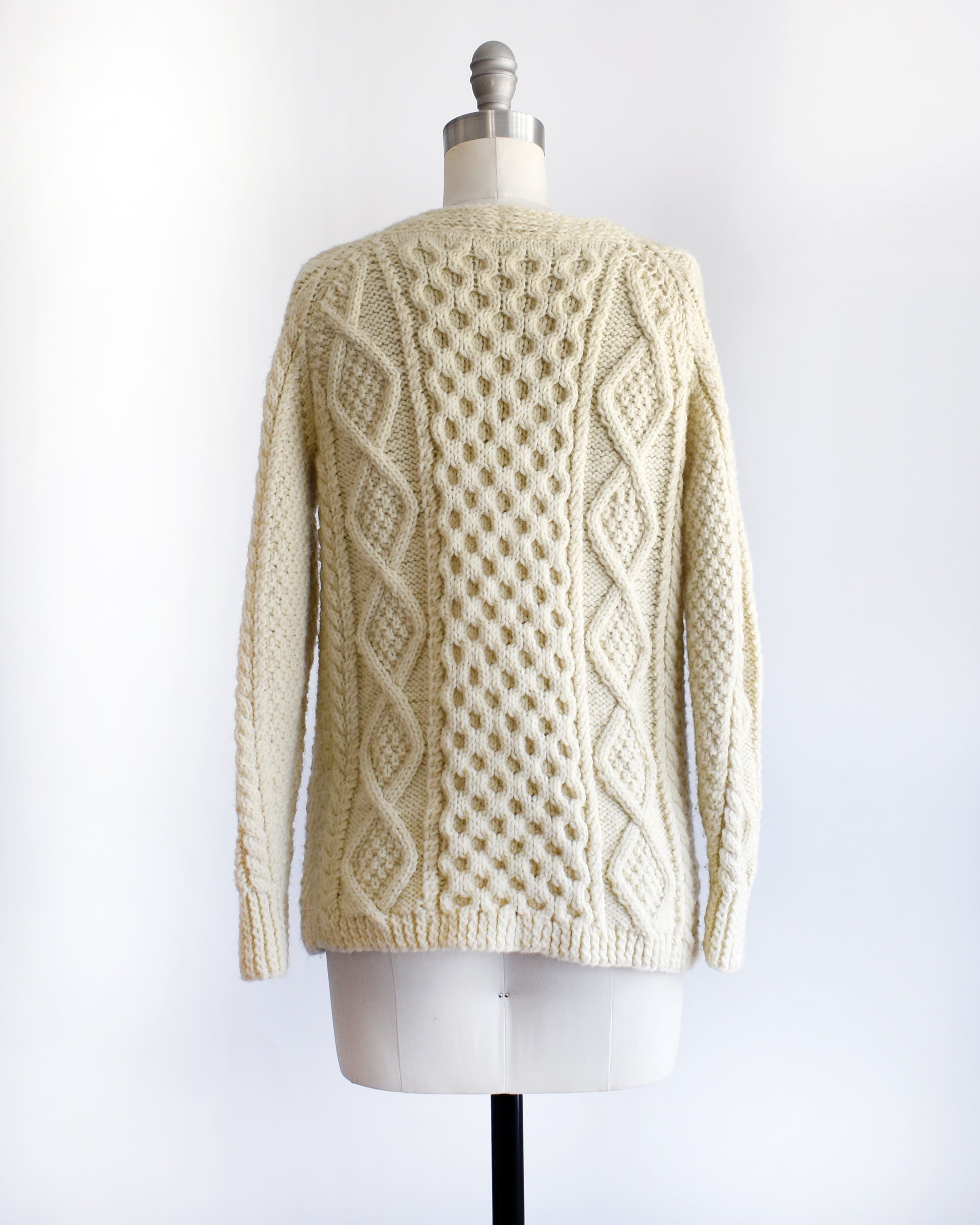 back view of a vintage 1970s/1980s cream-colored cable knit cardigan on a mannequin against a white background