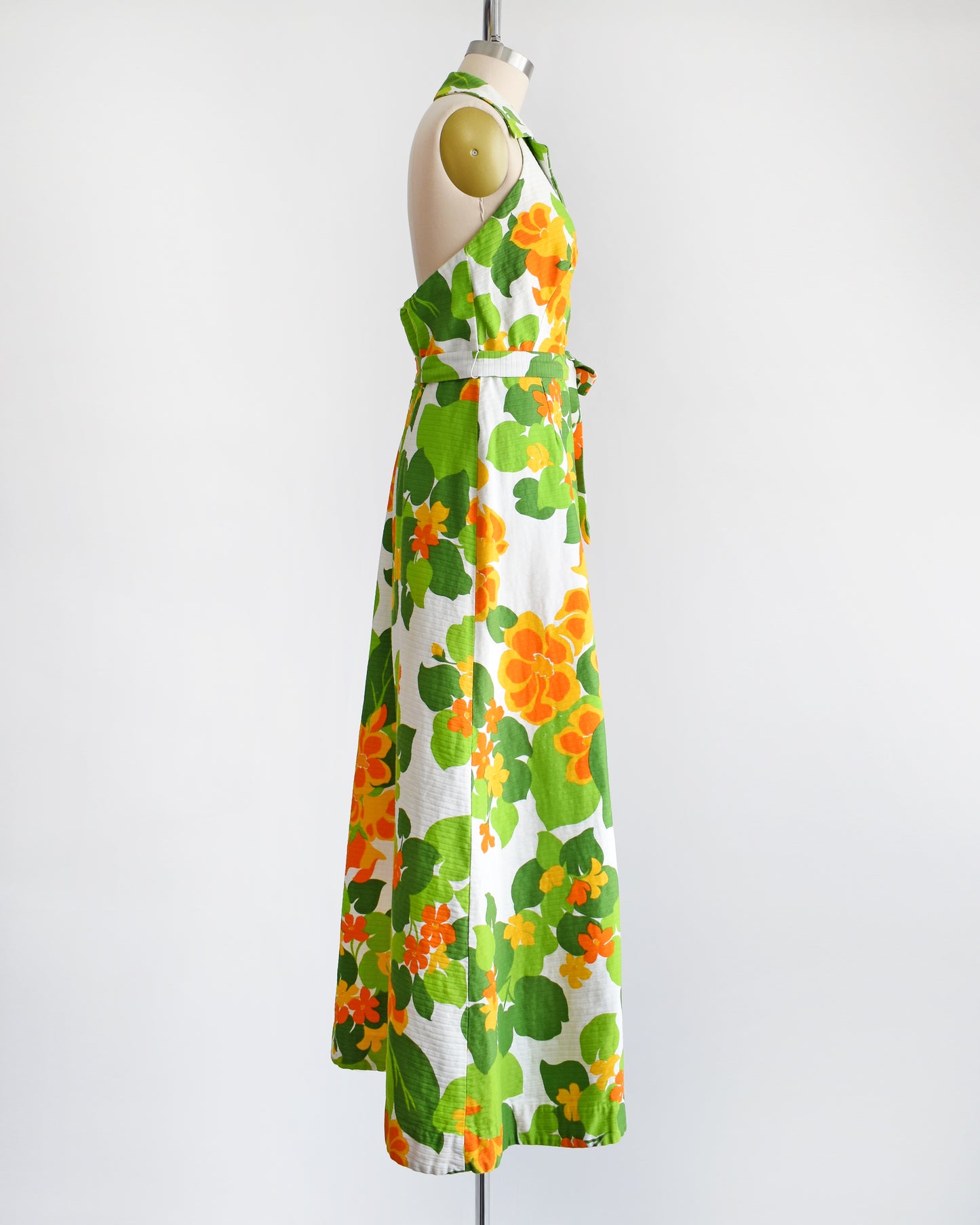 side view of a vintage 1970s white maxi dress by Malia that has a large orange and green floral print, collared neckline, button front, and matching belt.