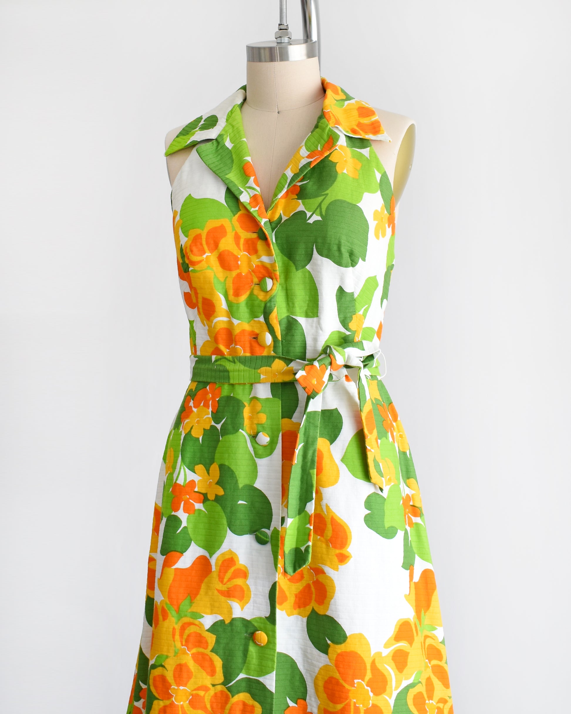 side front view of a vintage 1970s white maxi dress by Malia that has a large orange and green floral print, collared neckline, button front, and matching belt.