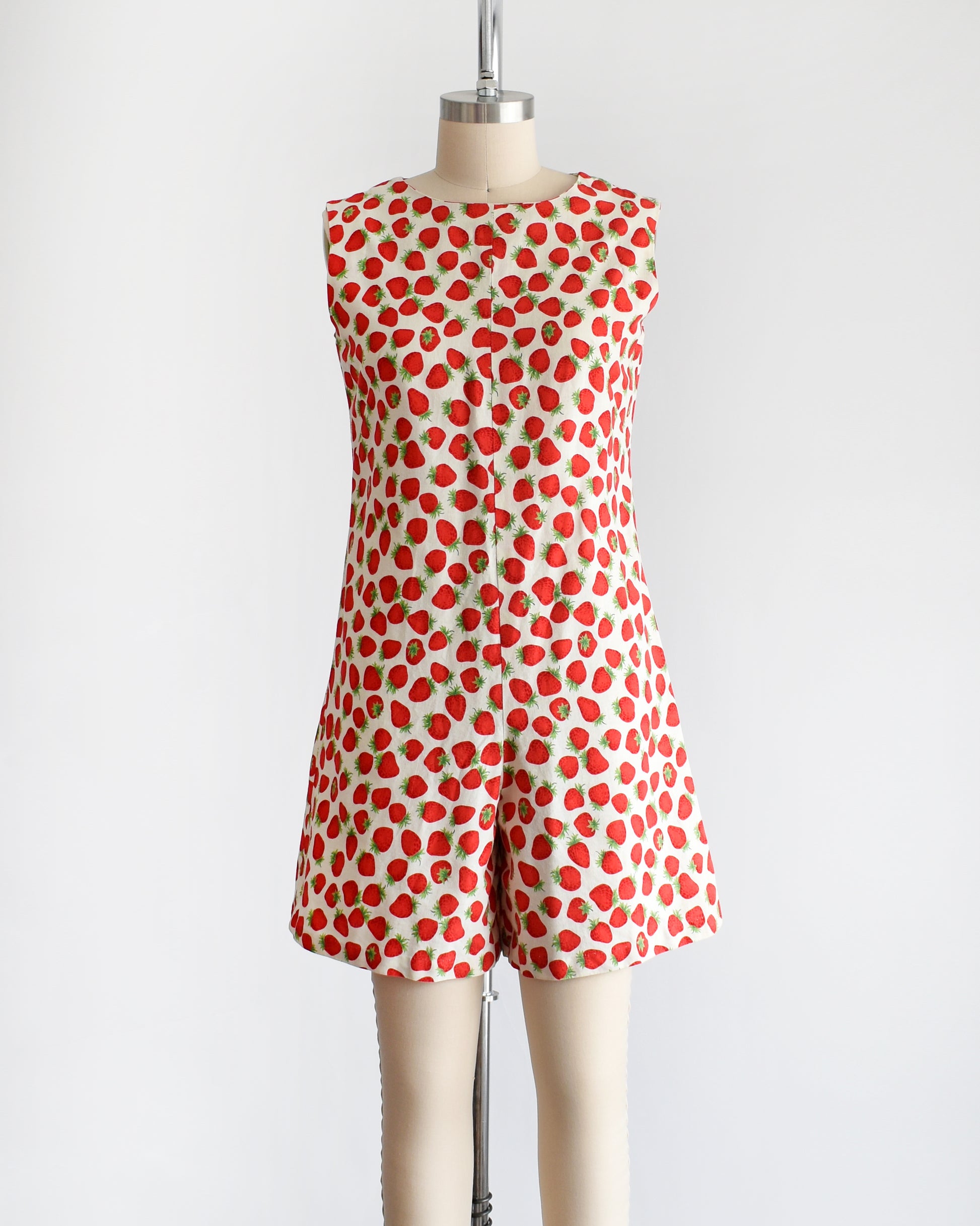 a vintage 1960s white romper with a red and green strawberry print. the romper is modeled on a dress form.