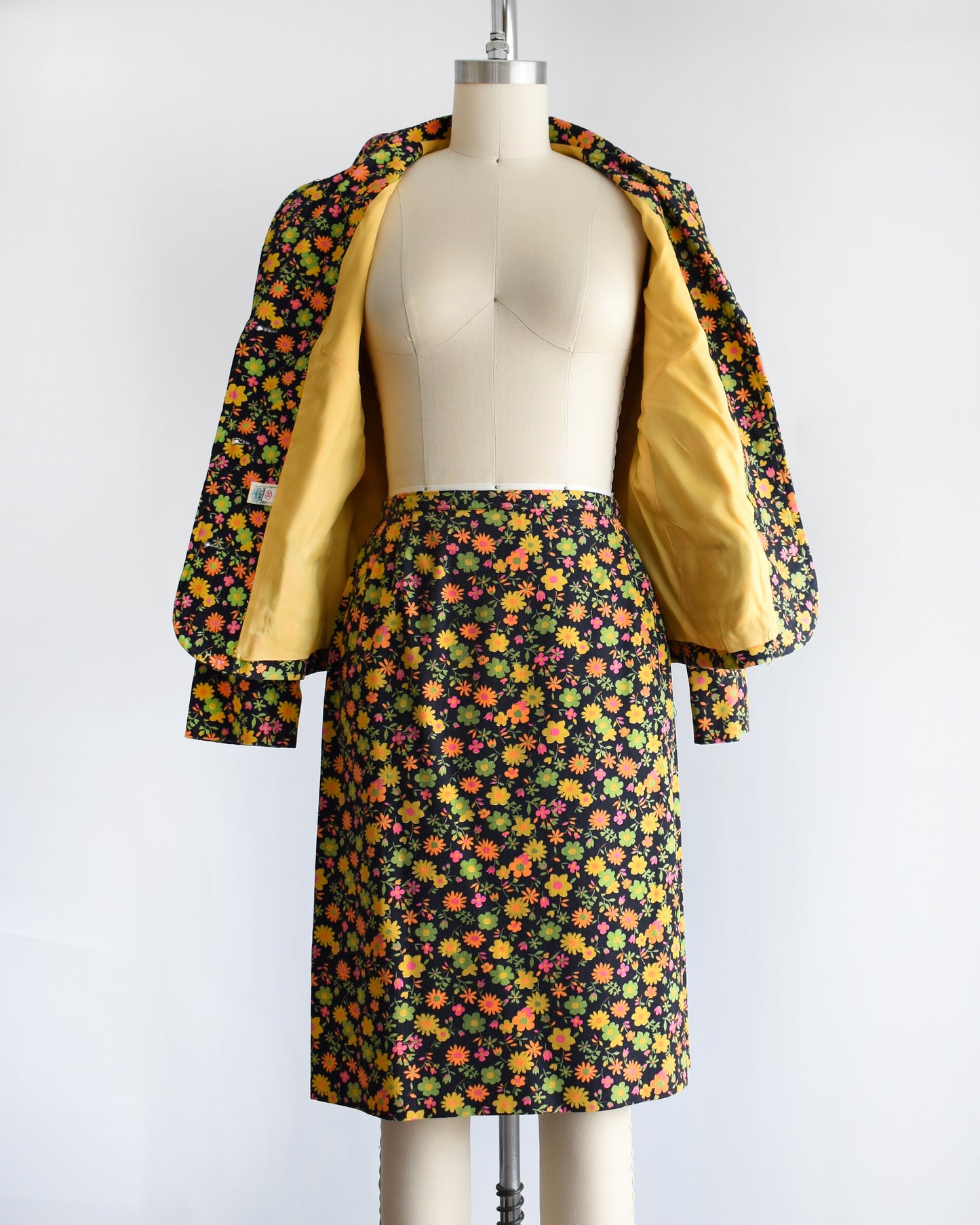 a vintage 1960s/1970s matching floral  blazer and skirt on a mannequin against a white background. the jacket is open showing the yellow lining