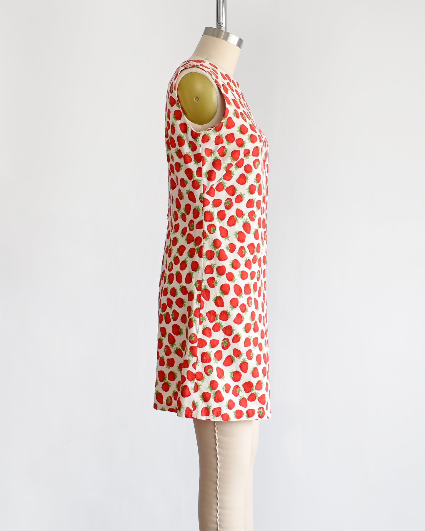 side view of a vintage 1960s white romper with a red and green strawberry print on a dress form.