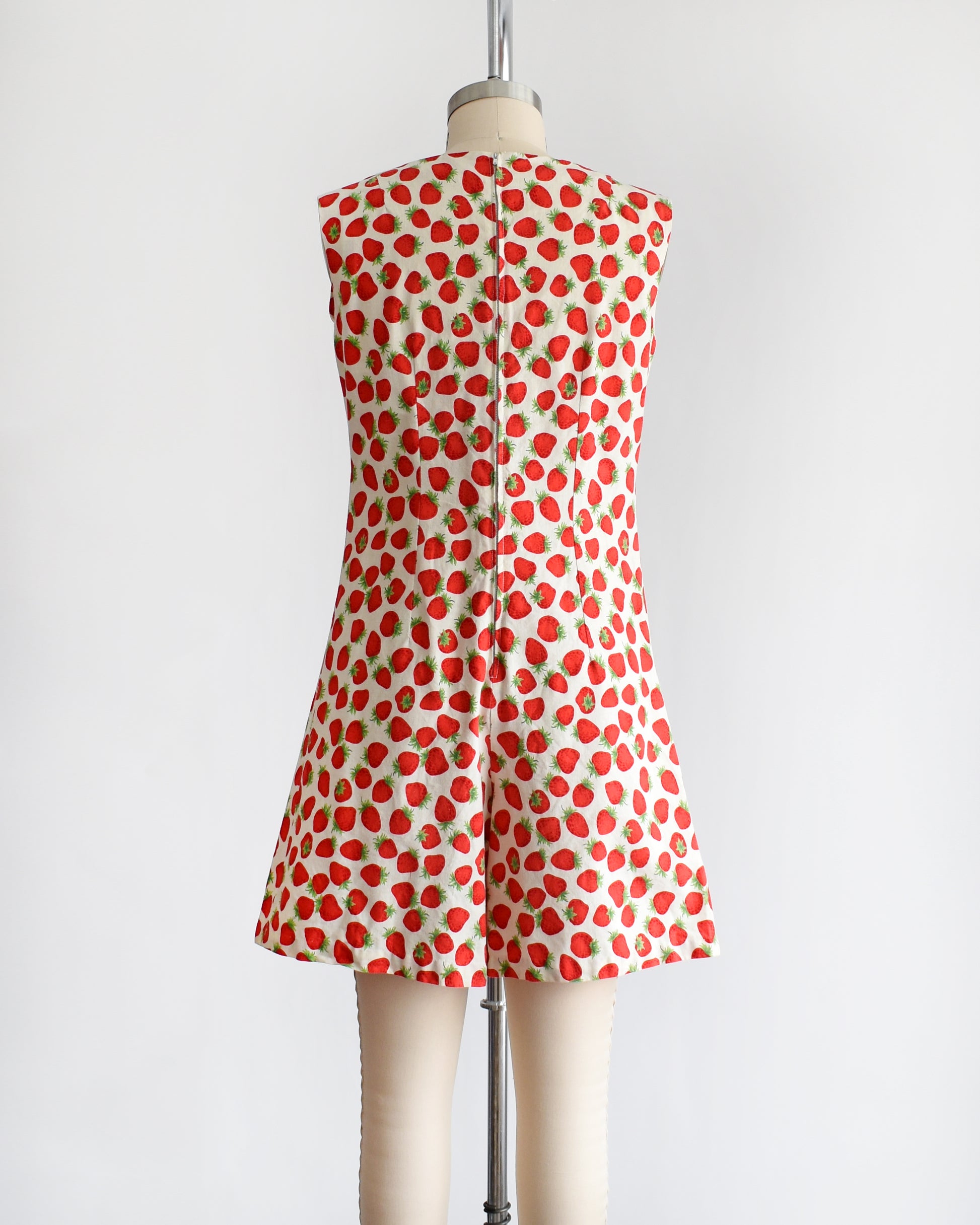 back view of a vintage 1960s white romper with a red and green strawberry print on a dress form.