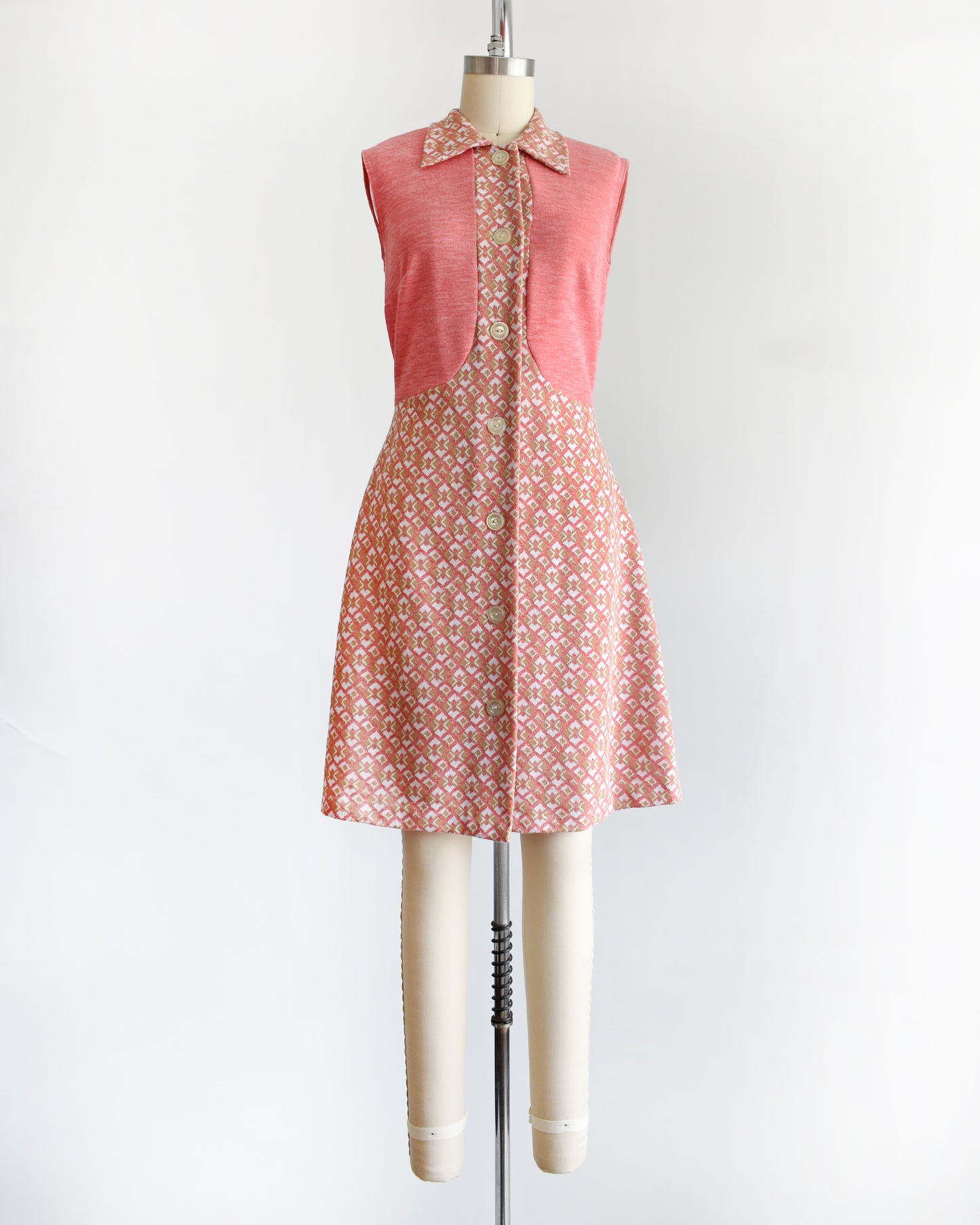a vintage 1960s/1970s pink sleeveless dress with a geometric pattern on a mannequin against a white background