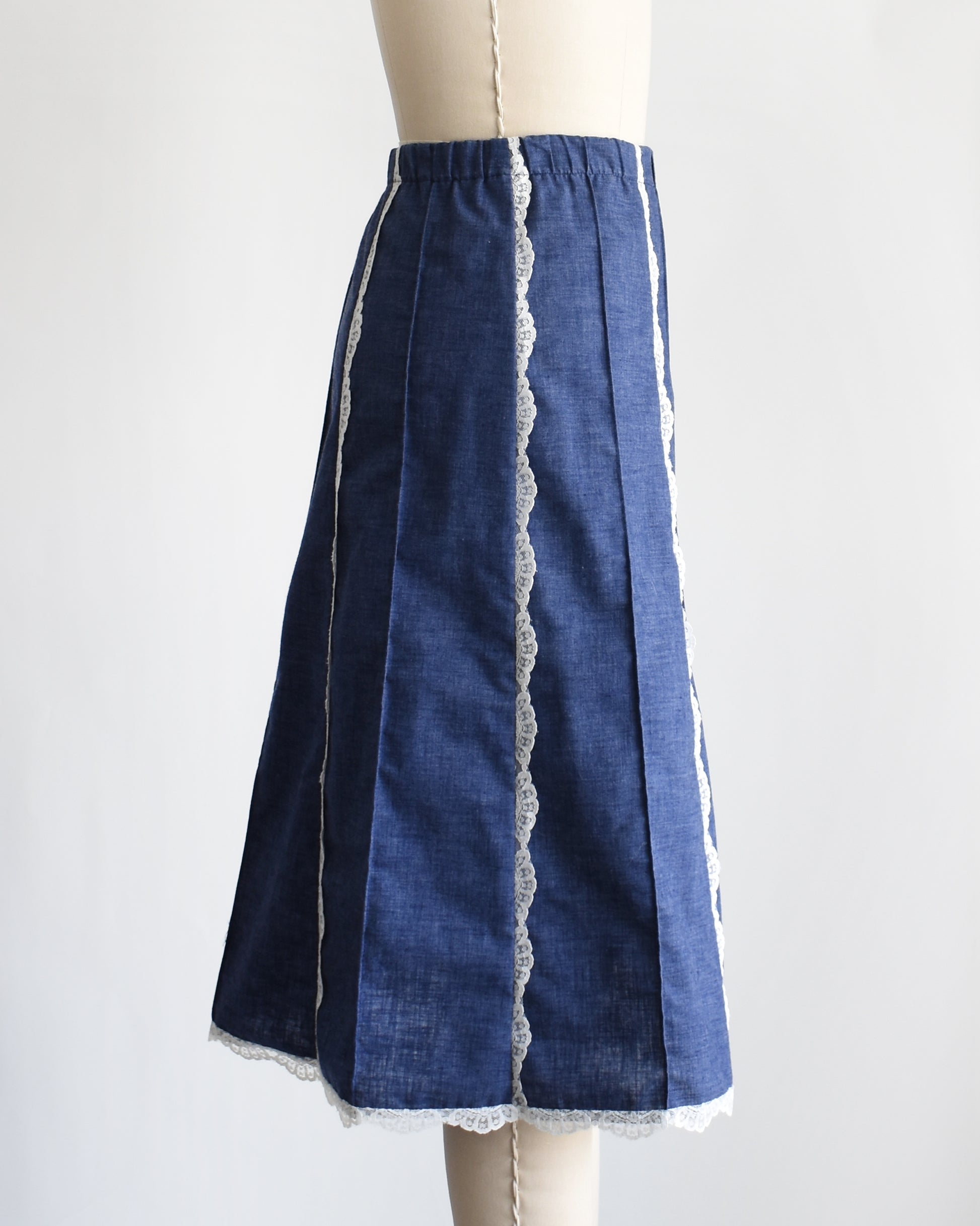side view of a vintage 1970s blue chambray lace skirt on a dress form against a white background