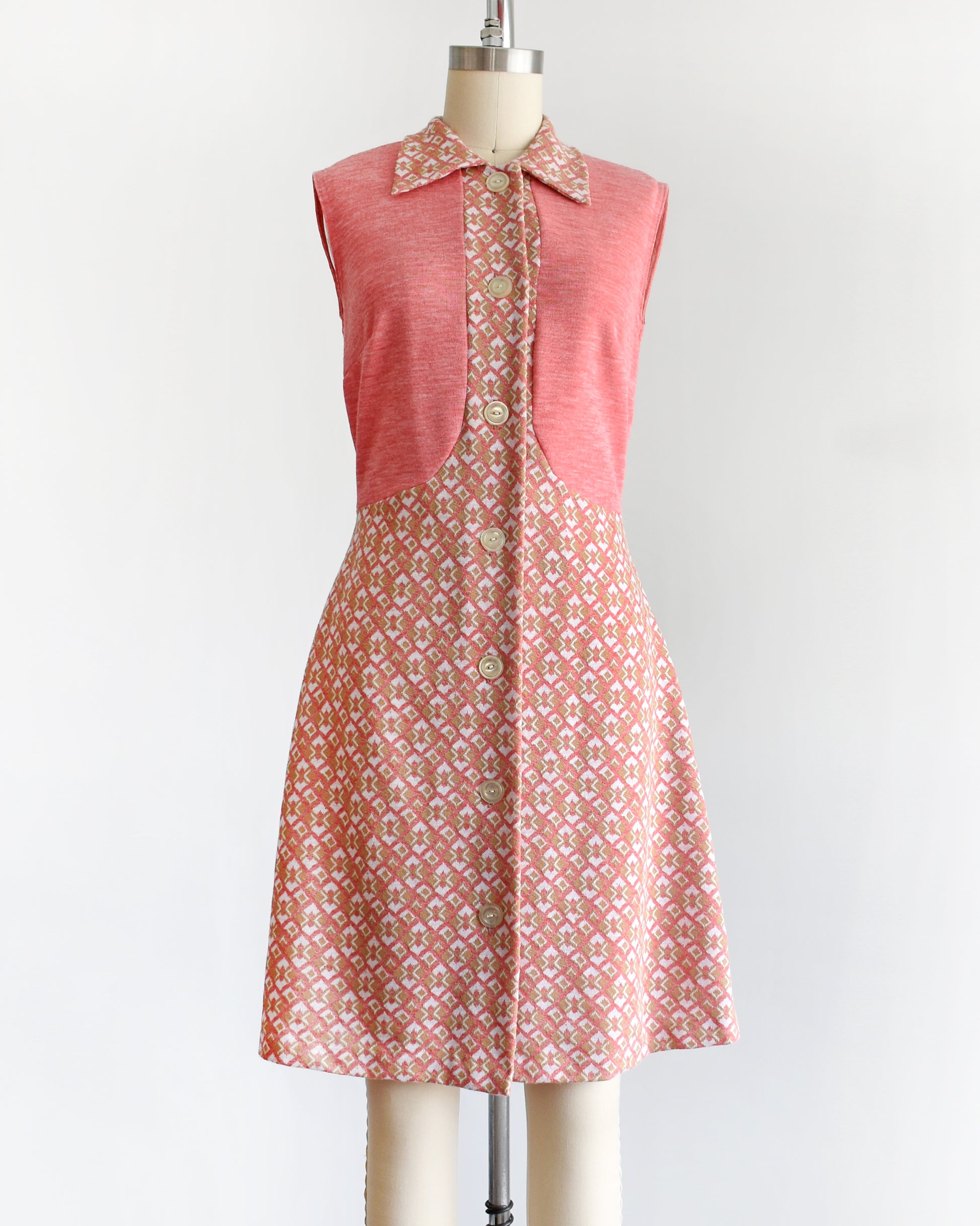a vintage 1960s/1970s pink sleeveless dress with a geometric pattern on a mannequin against a white background
