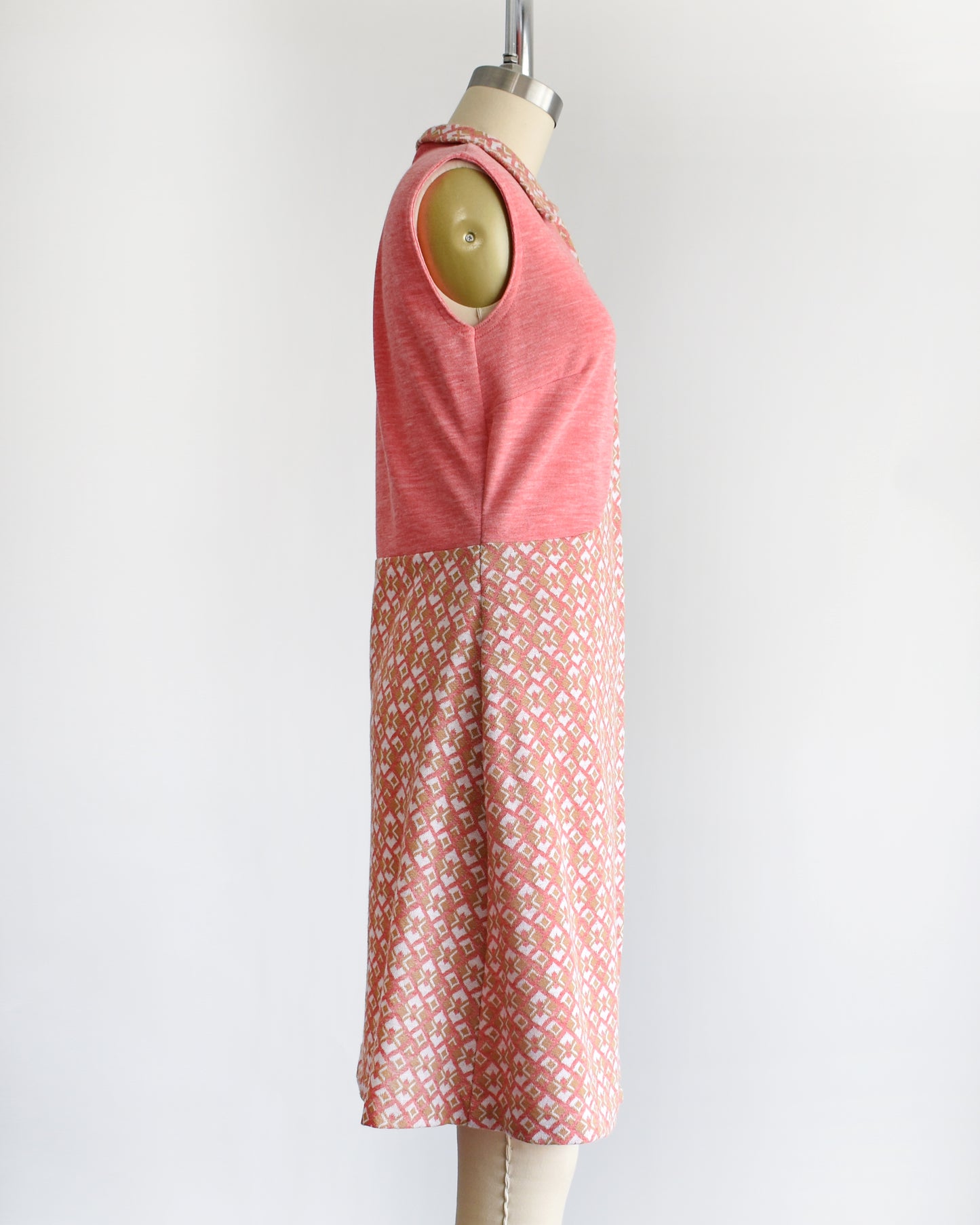 side view of a vintage 1960s/1970s pink sleeveless dress with a geometric pattern on a mannequin against a white background