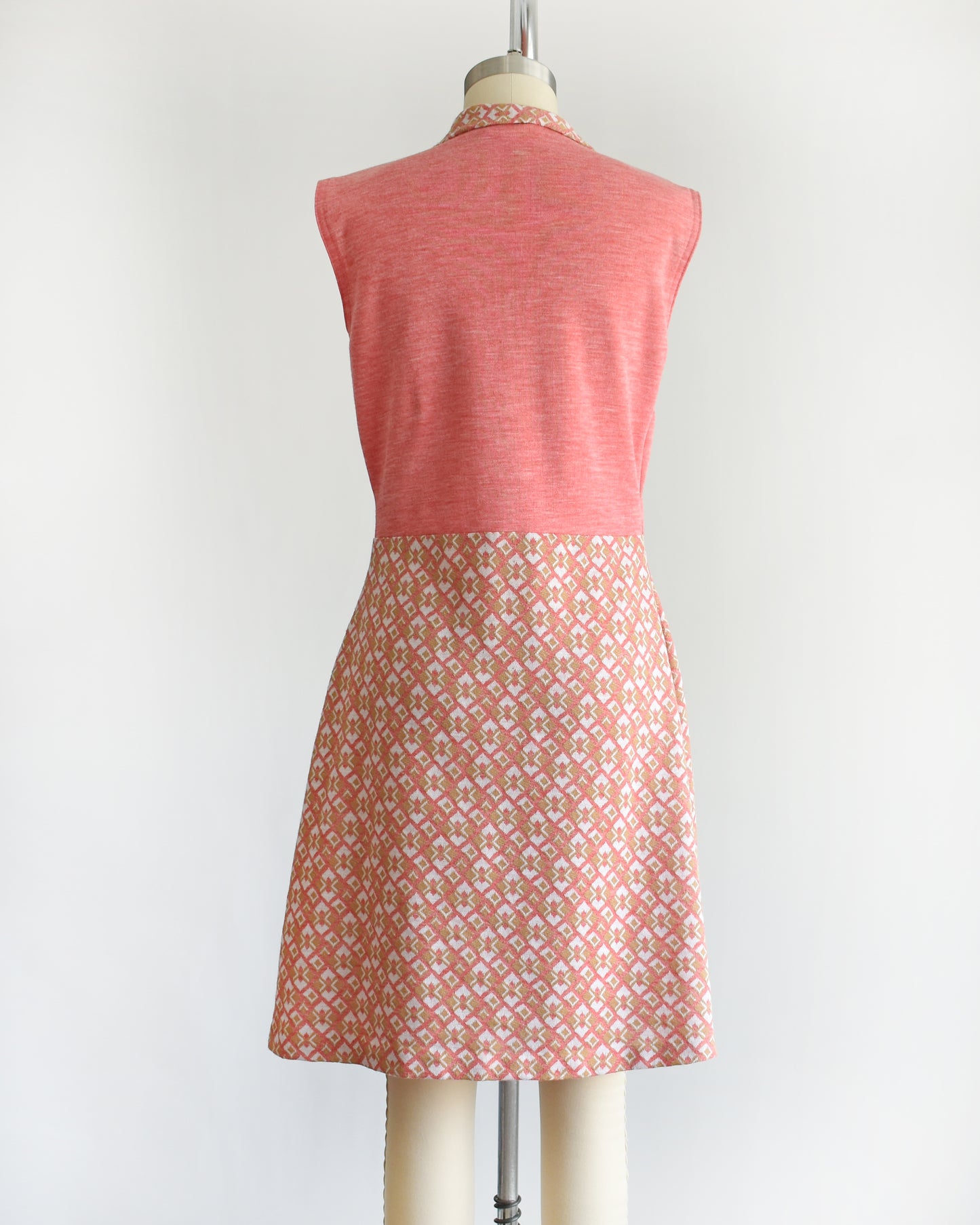 back view of a vintage 1960s/1970s pink sleeveless dress with a geometric pattern on a mannequin against a white background