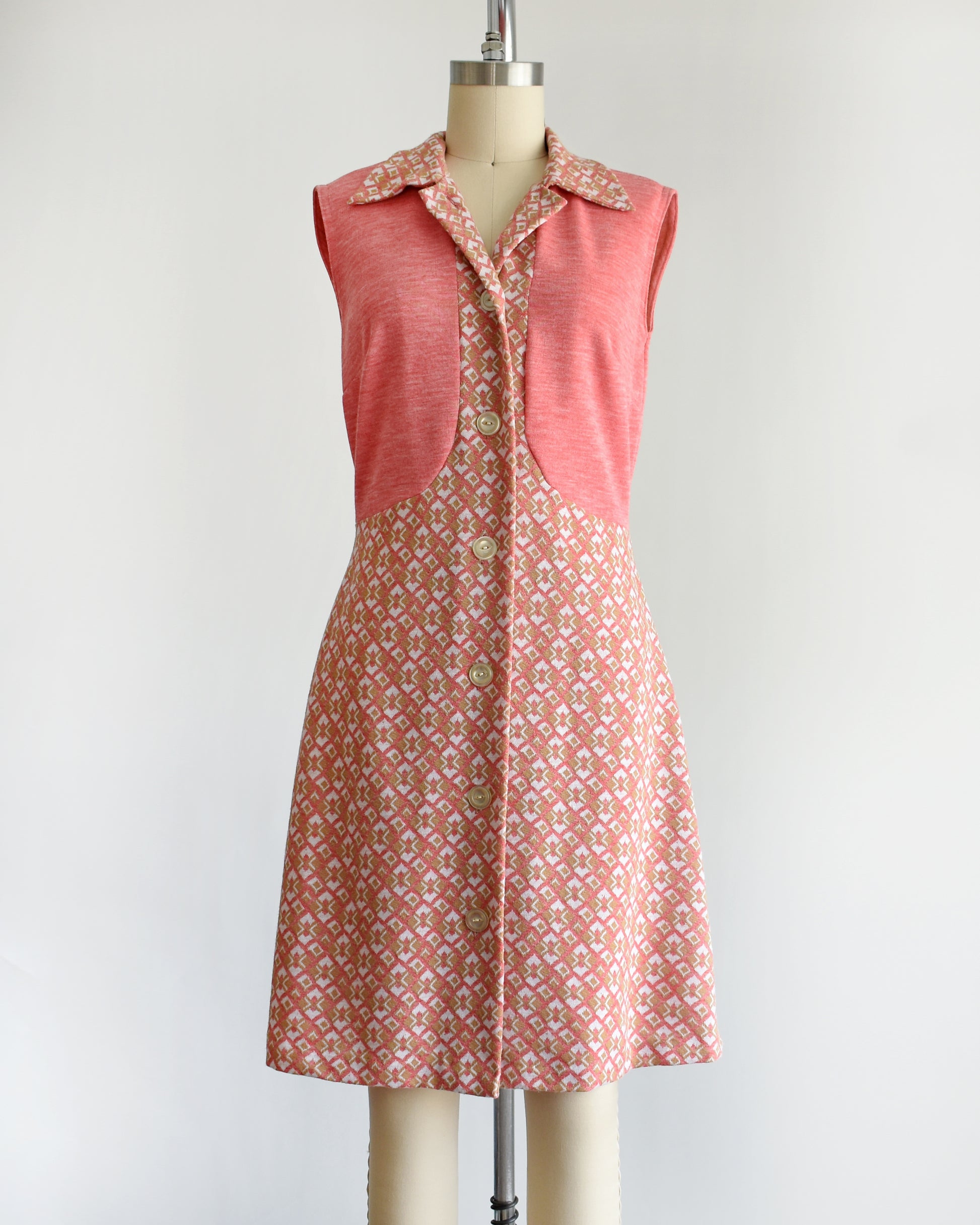 a vintage 1960s/1970s pink sleeveless dress with a geometric pattern on a mannequin against a white background
