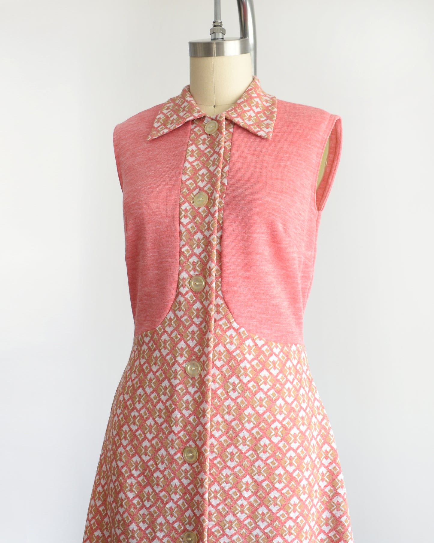 side view of a vintage 1960s/1970s pink sleeveless dress with a geometric pattern on a mannequin against a white background