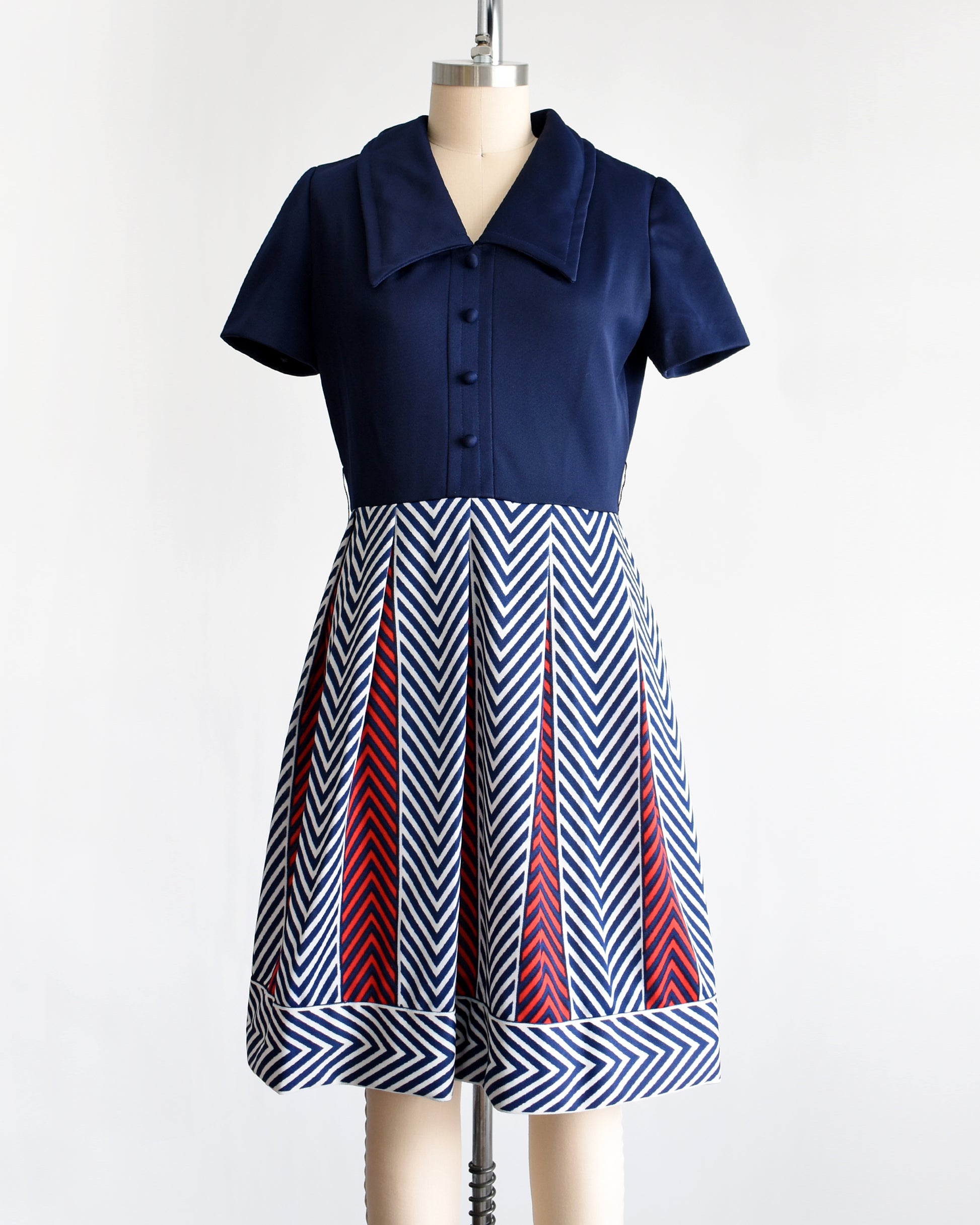 a vintage 1970s navy blue, white, and red dress with a chevron patterned skirt on a mannequin against a white background
