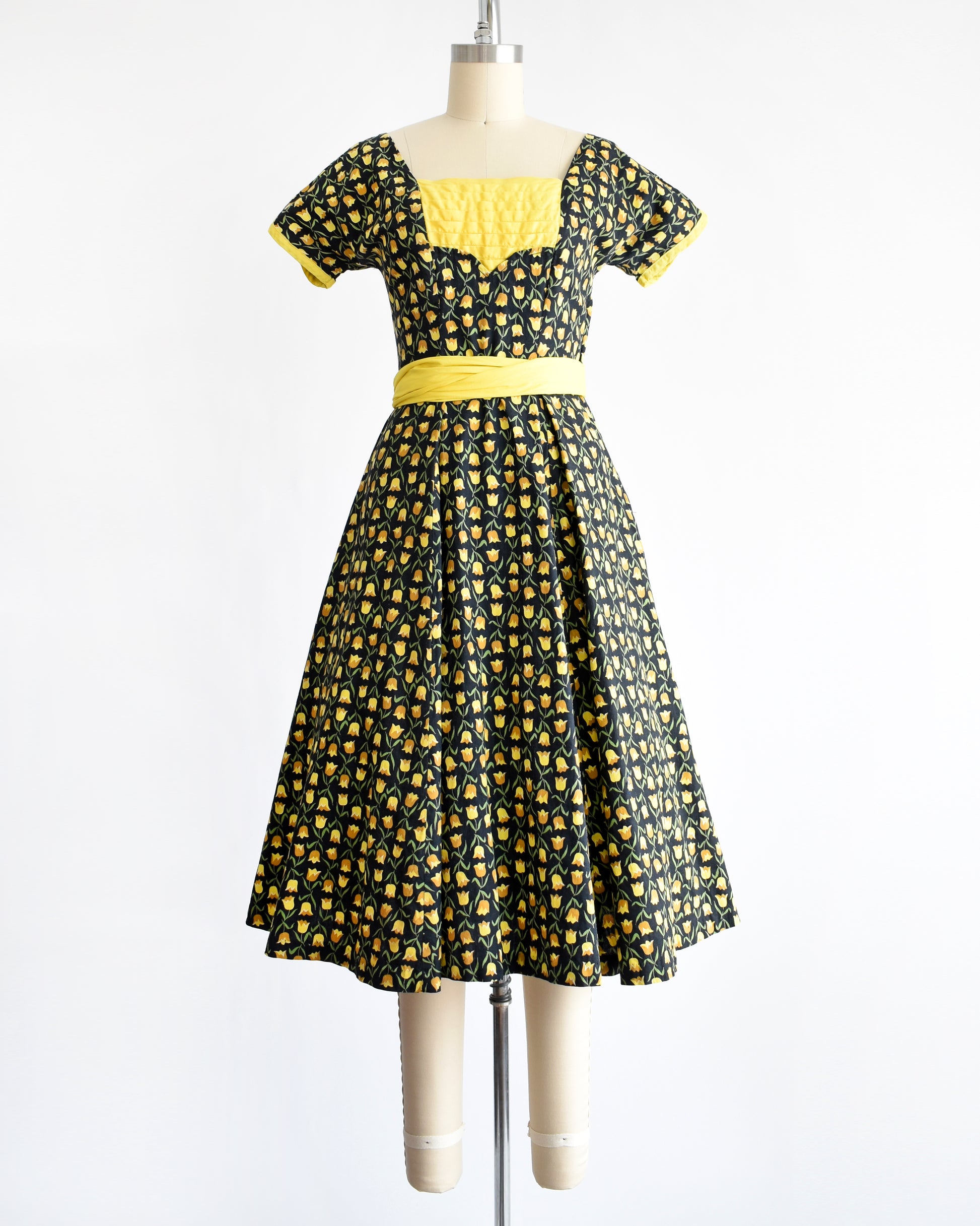 a vintage 1950s black fit and flare dress with a yellow floral print and yellow waist sash