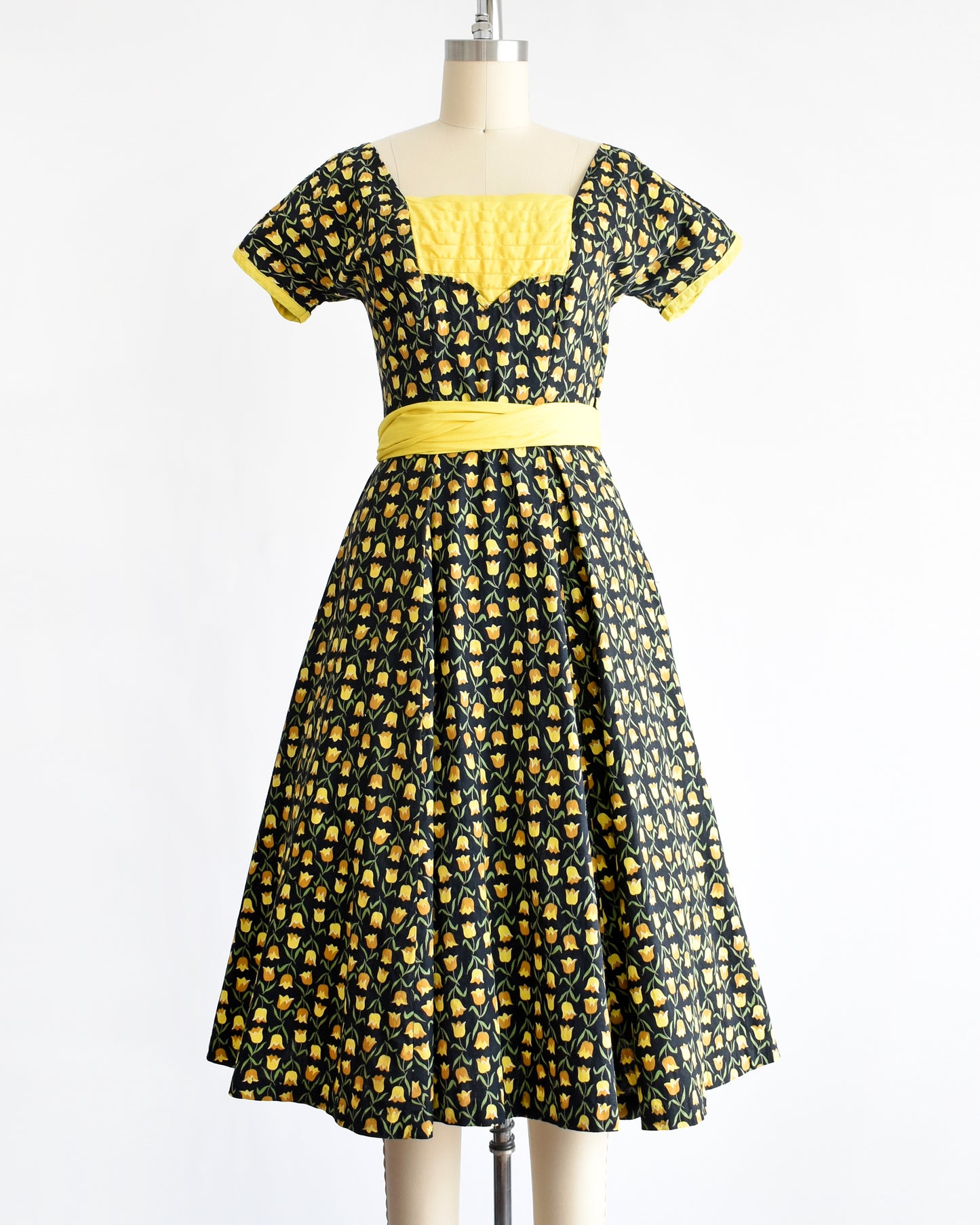 a vintage 1950s black fit and flare dress with a yellow floral print and yellow waist sash