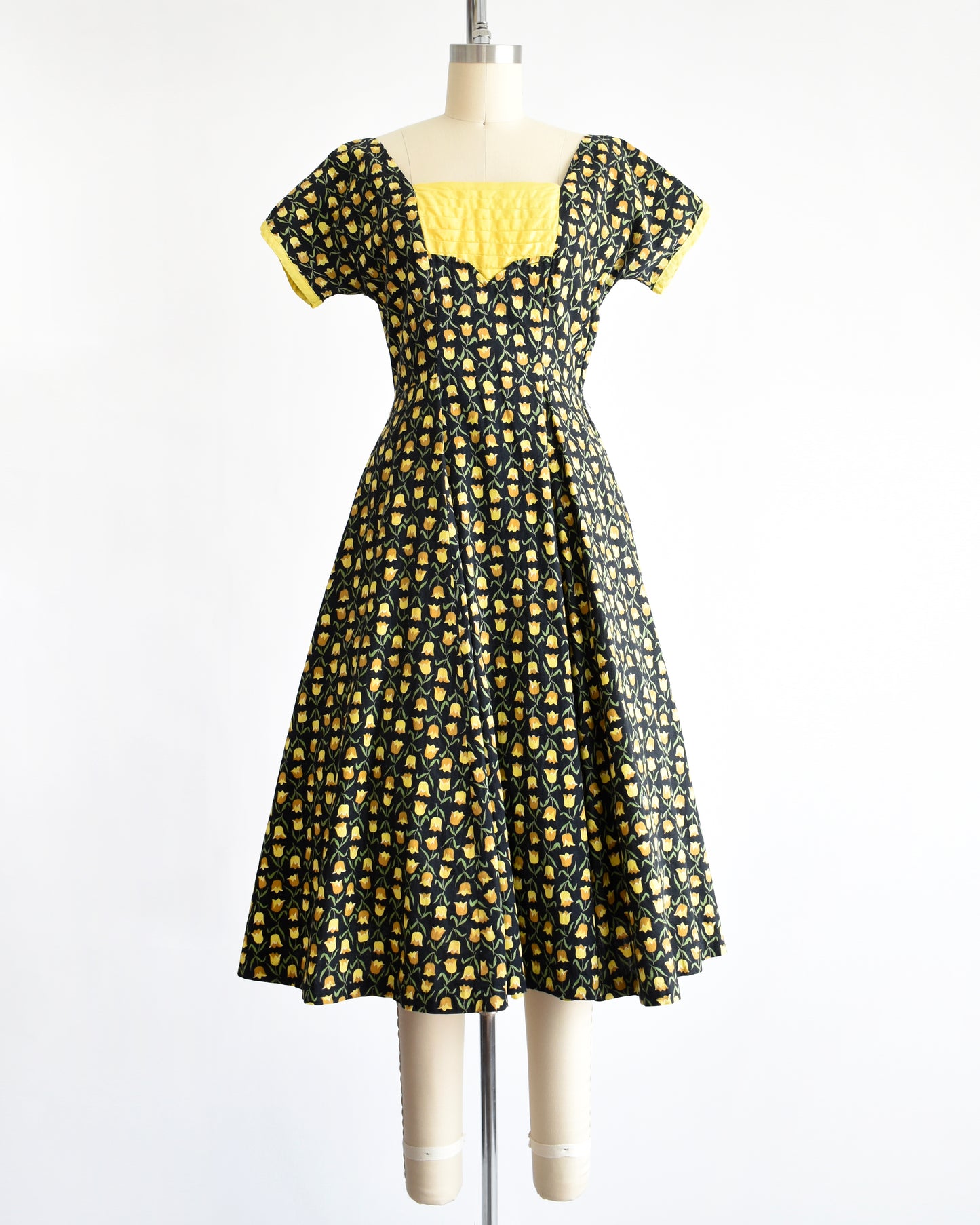 a vintage 1950s black fit and flare dress with a yellow floral print. the waist sash is tied in the back of the dress