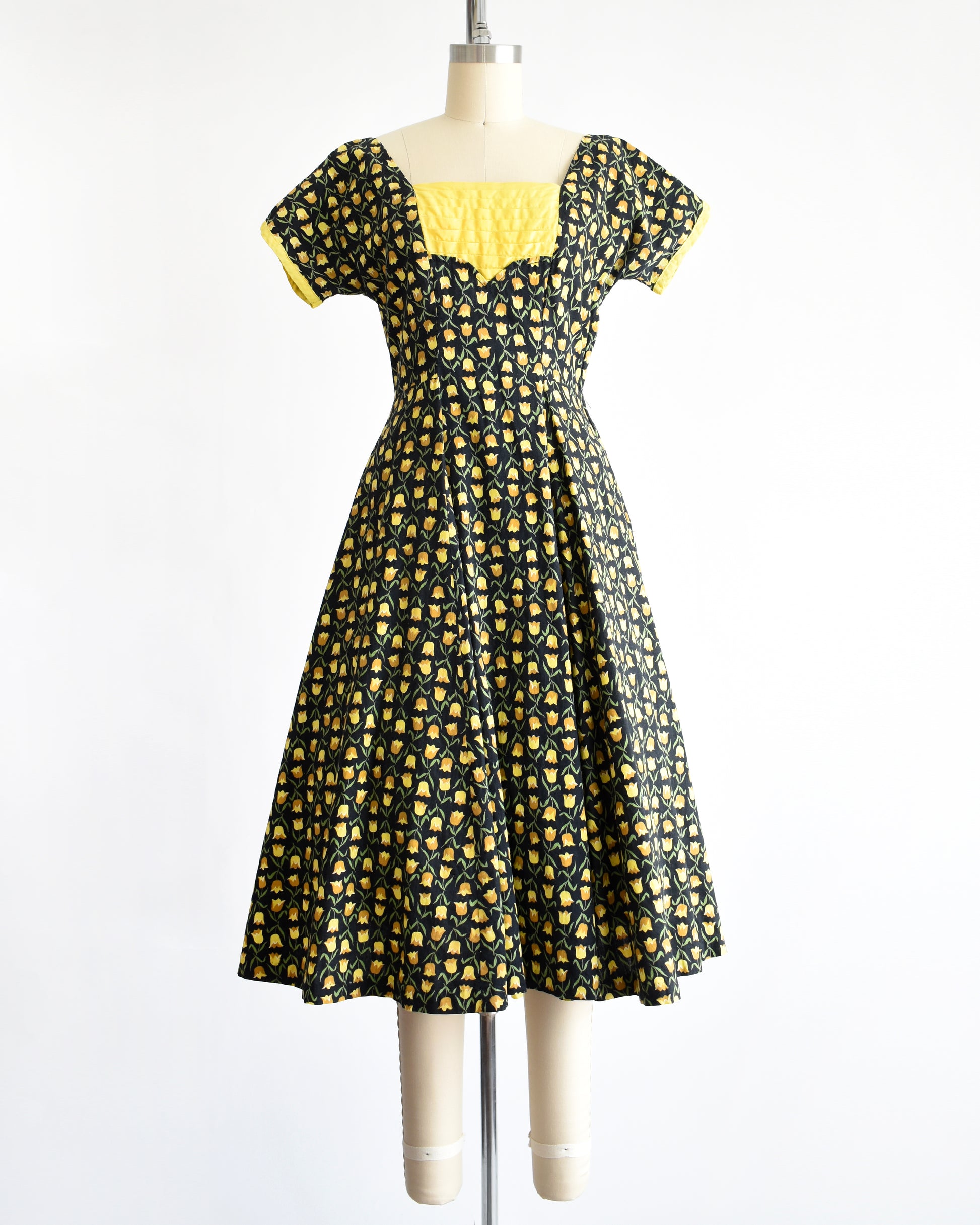 a vintage 1950s black fit and flare dress with a yellow floral print. the waist sash is tied in the back of the dress