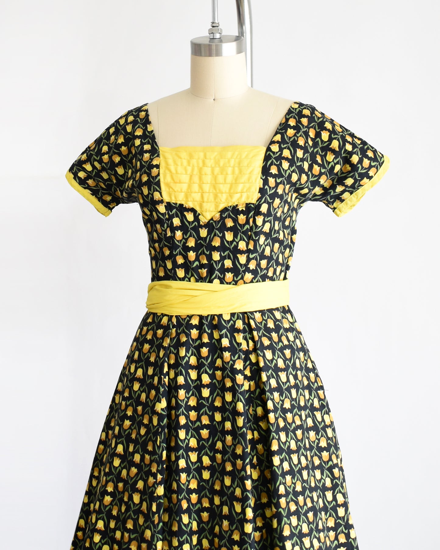 side front view of a vintage 1950s black and yellow floral print dress with yellow waist sash