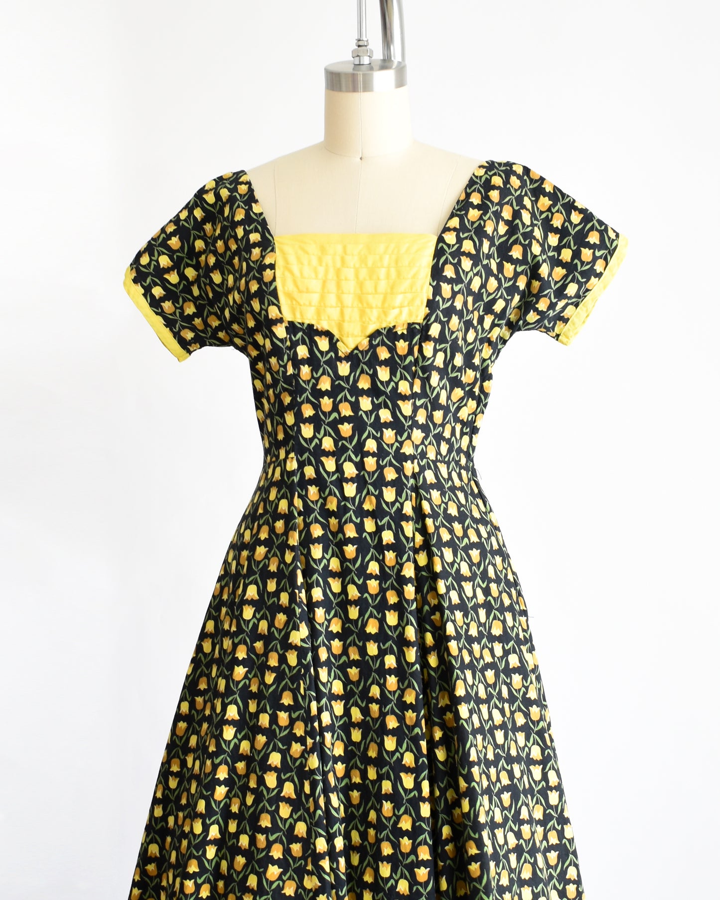 side front view of a vintage 1950s black and yellow floral print dress. the sash is tied in the back