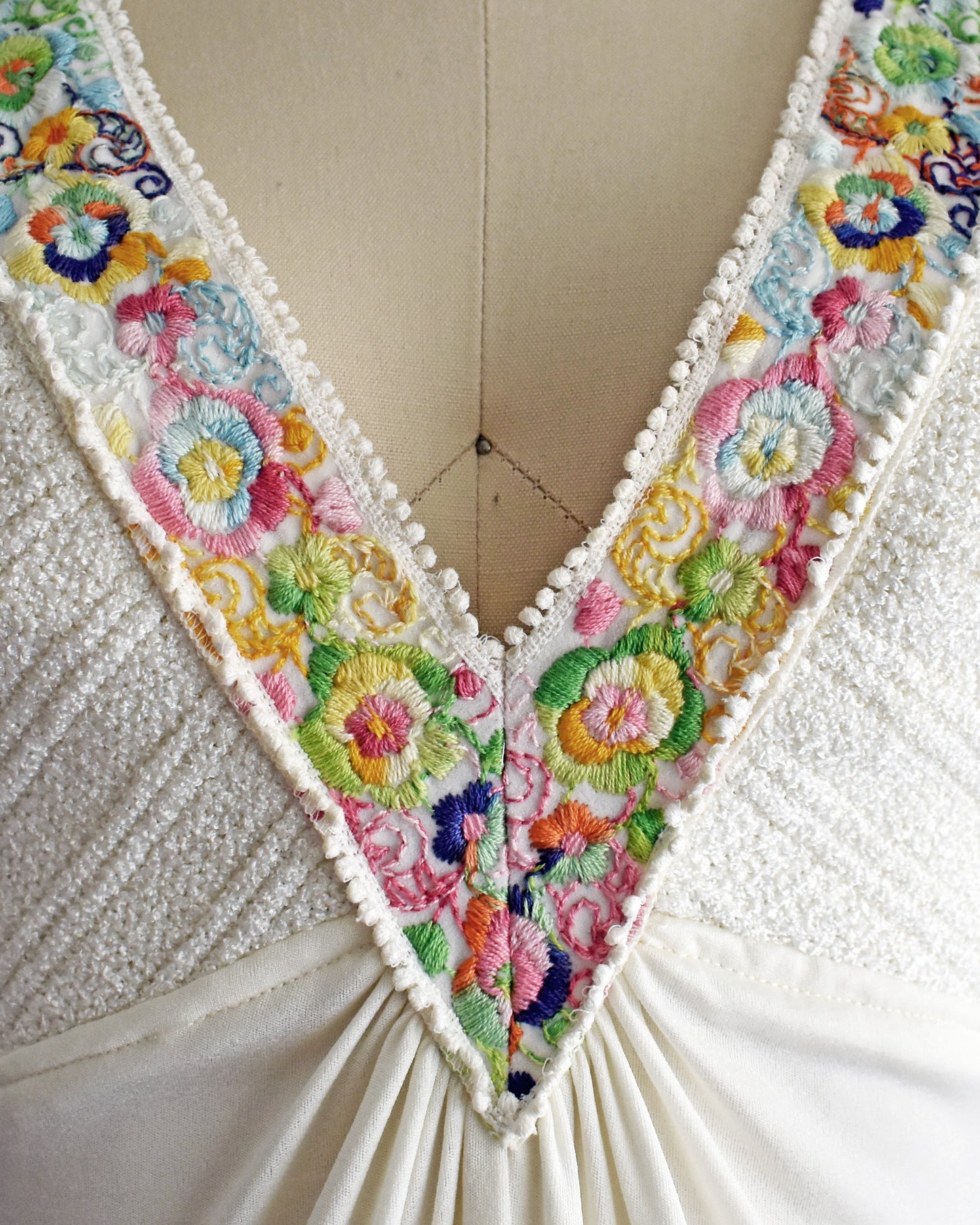 close up of the colorful floral embroidery on the straps that go down the front on a dress form against a white background