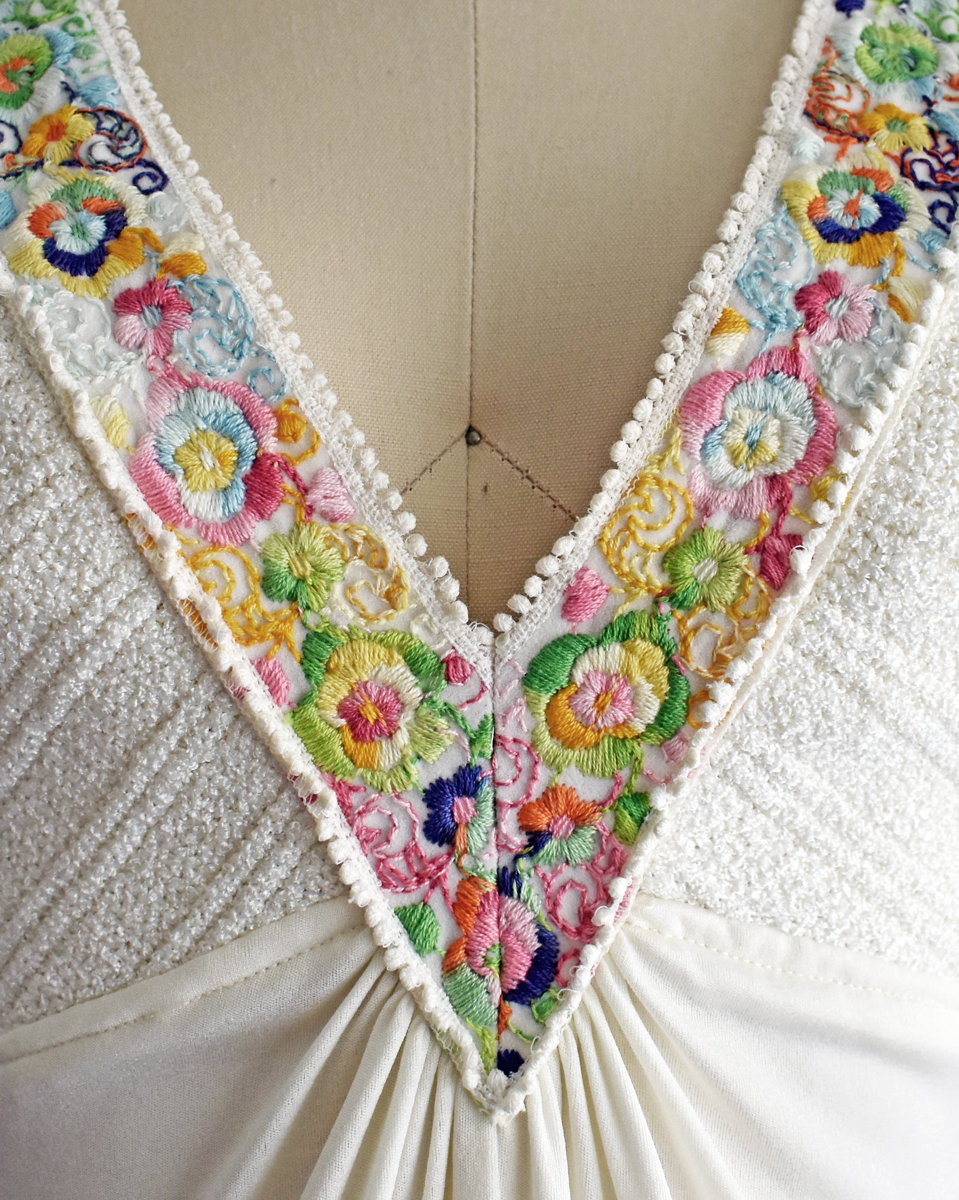 close up of the colorful floral embroidery on the straps that go down the front on a dress form against a white background