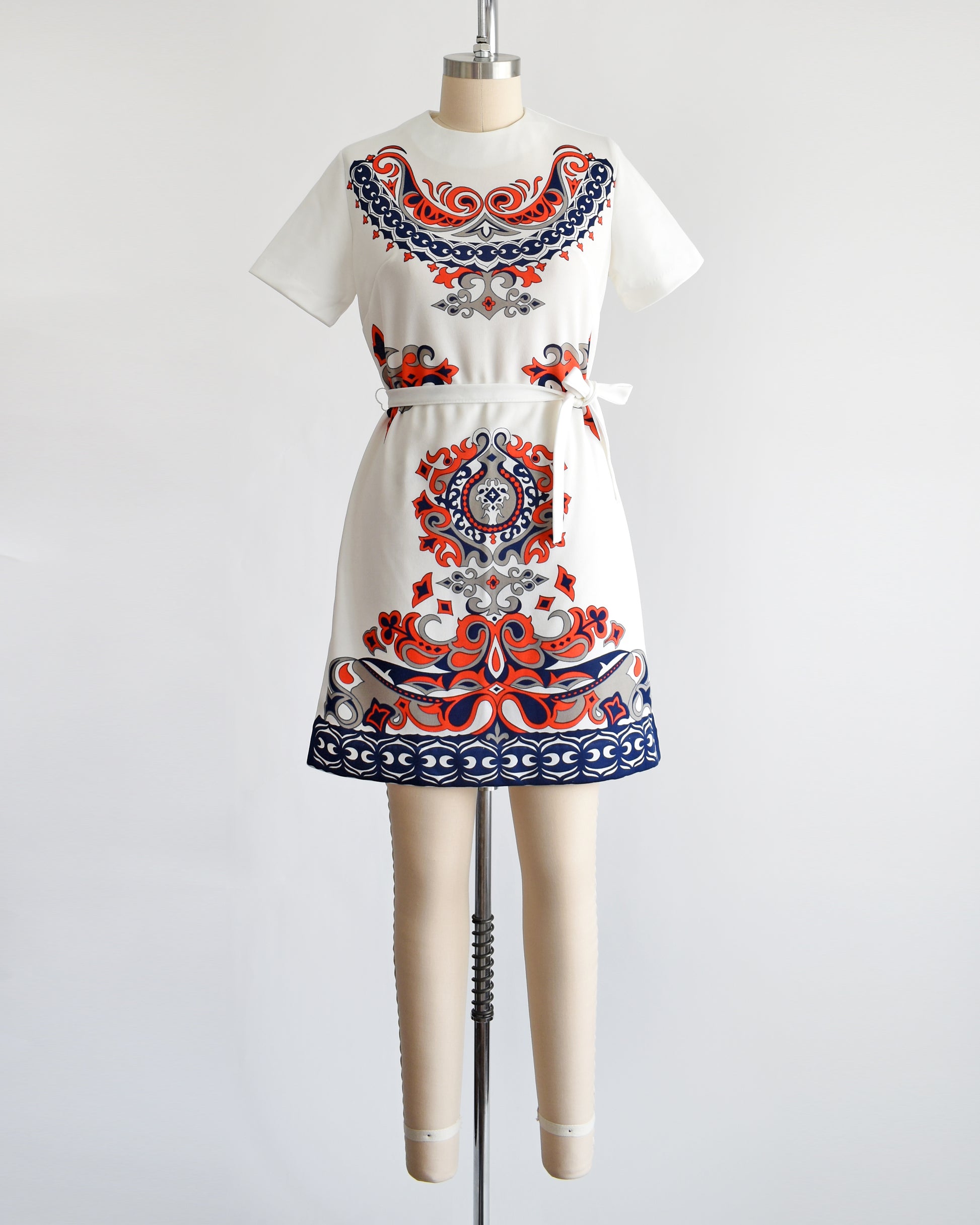 a vintage 1970s white mod dress that has a red, navy blue, and gray damask print on the front, sides, and back. the dress comes with a matching white tie belt