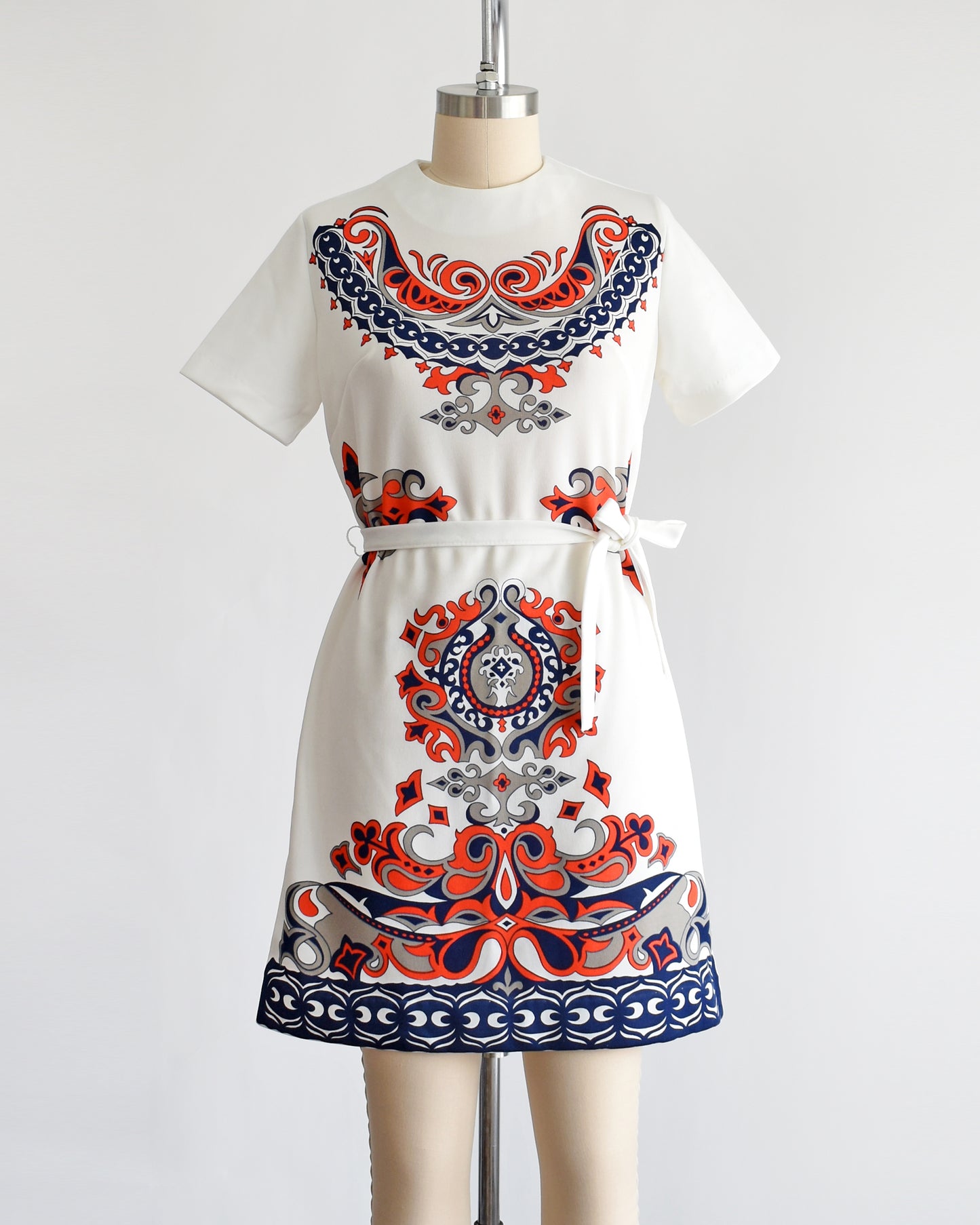 a vintage 1970s white mod dress that has a red, navy blue, and gray damask print on the front, sides, and back. the dress comes with a matching white tie belt