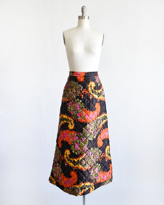 a vintage 1970s black quilted skit that has a colorful floral and paisley print on a mannequin against a white background