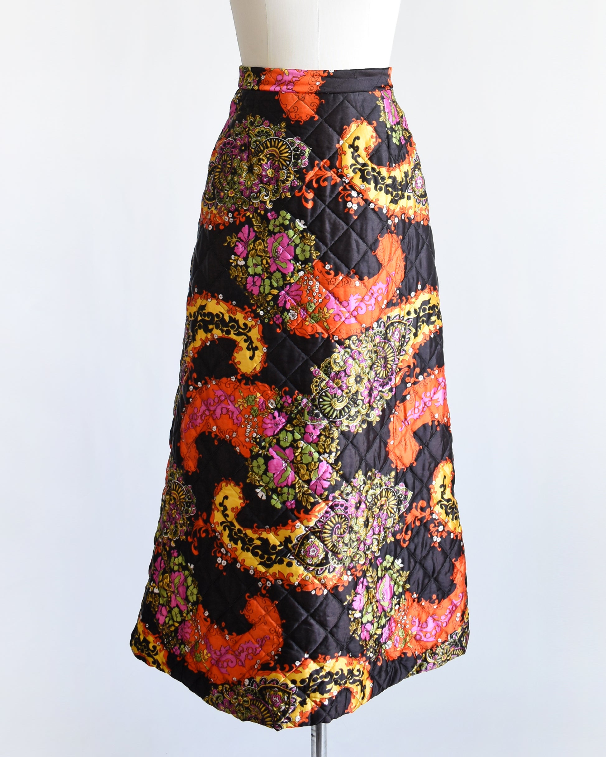a vintage 1970s black quilted skit that has a colorful floral and paisley print on a mannequin against a white background