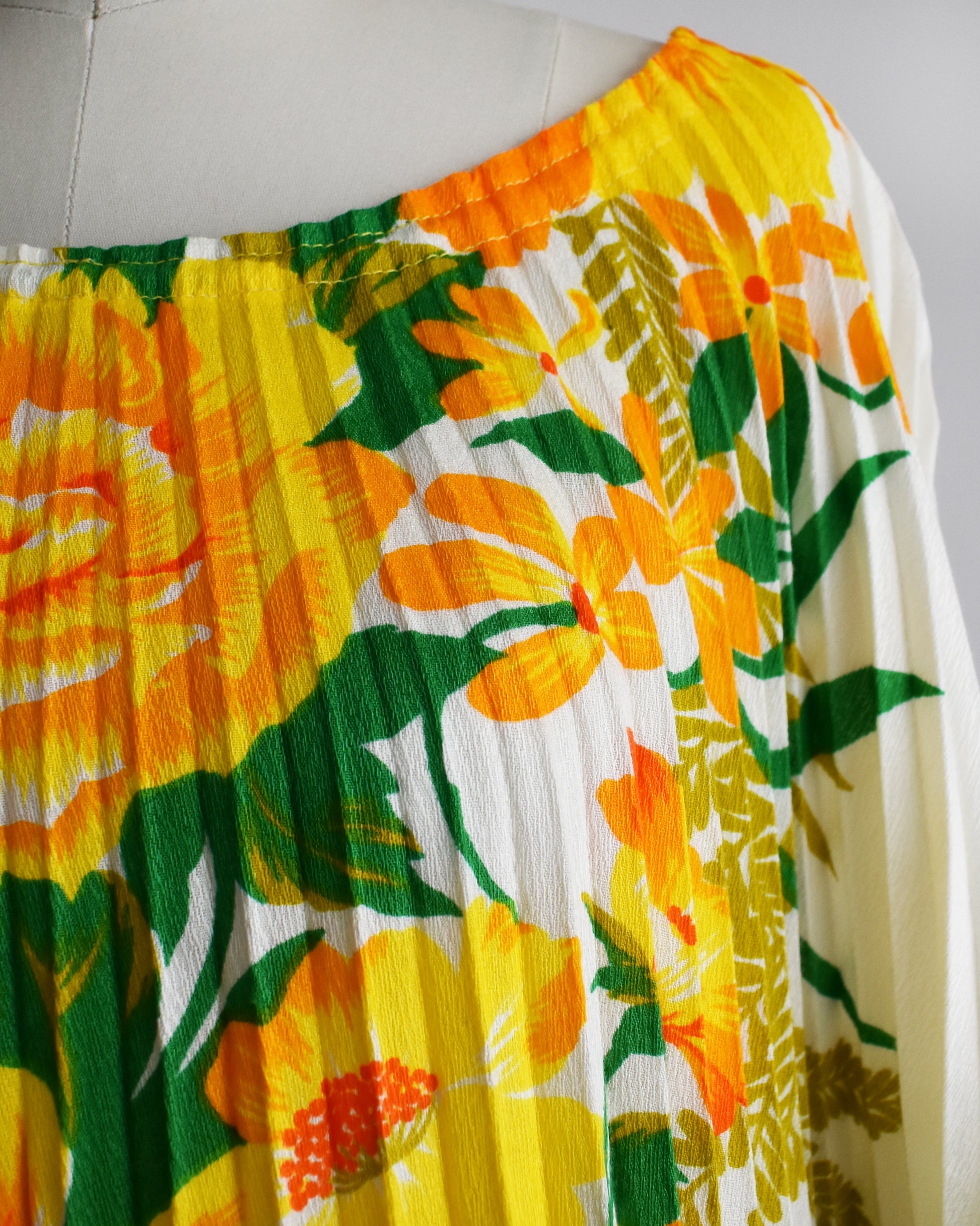 close up of the floral print on a vintage 1970s floral kaftan blouse on a dress form against a white background