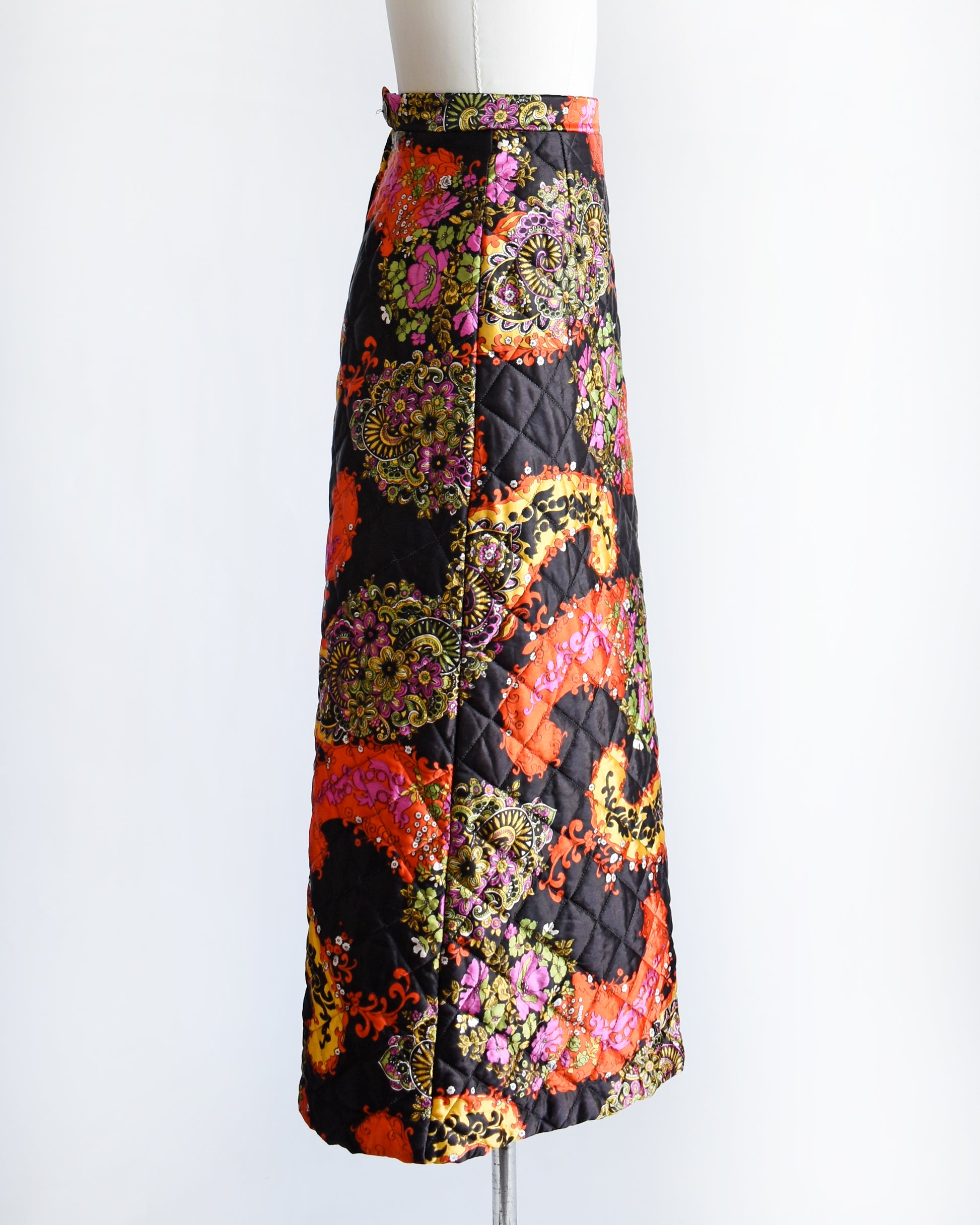 side view of a vintage 1970s black quilted skit that has a colorful floral and paisley print on a mannequin against a white background