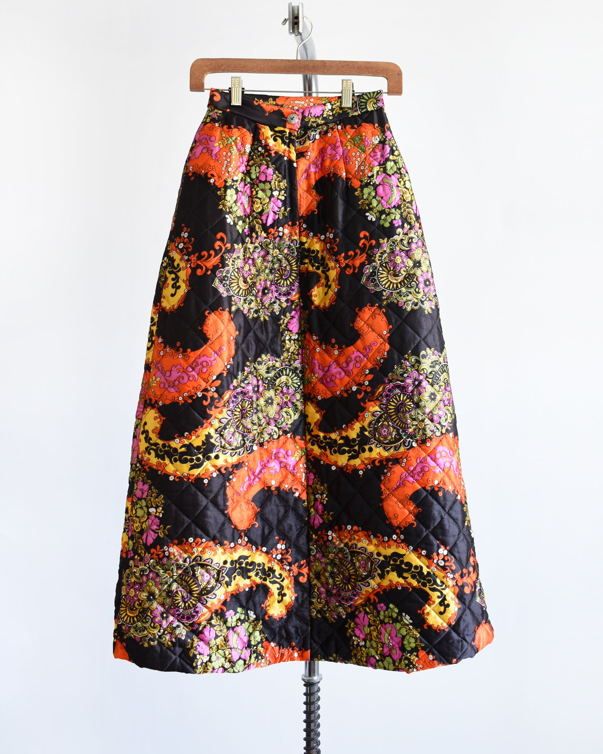 back view of a vintage 1970s black quilted skit that has a colorful floral and paisley print on a hanger
