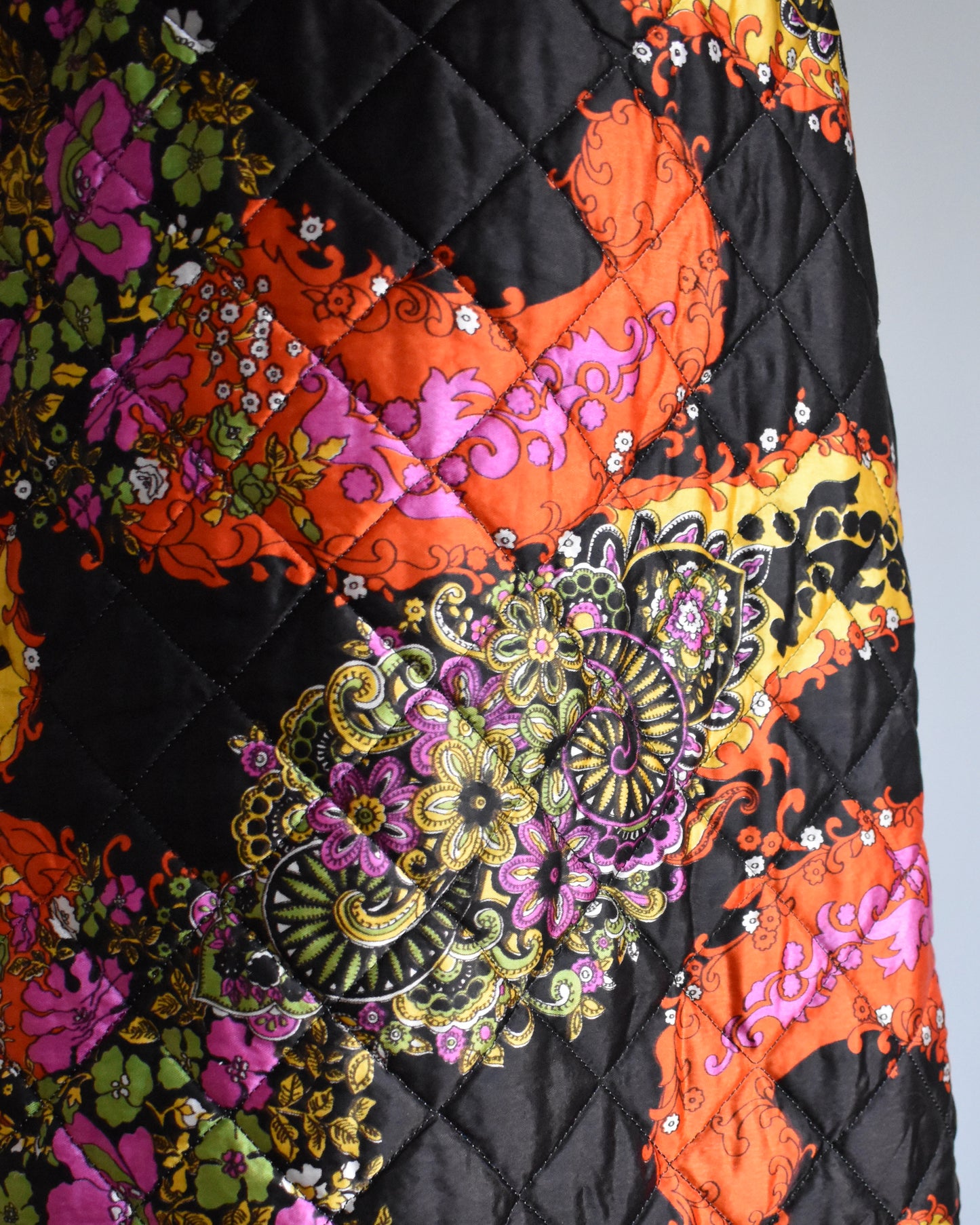 close up of a vintage 1970s black quilted skit that has a colorful floral and paisley print 