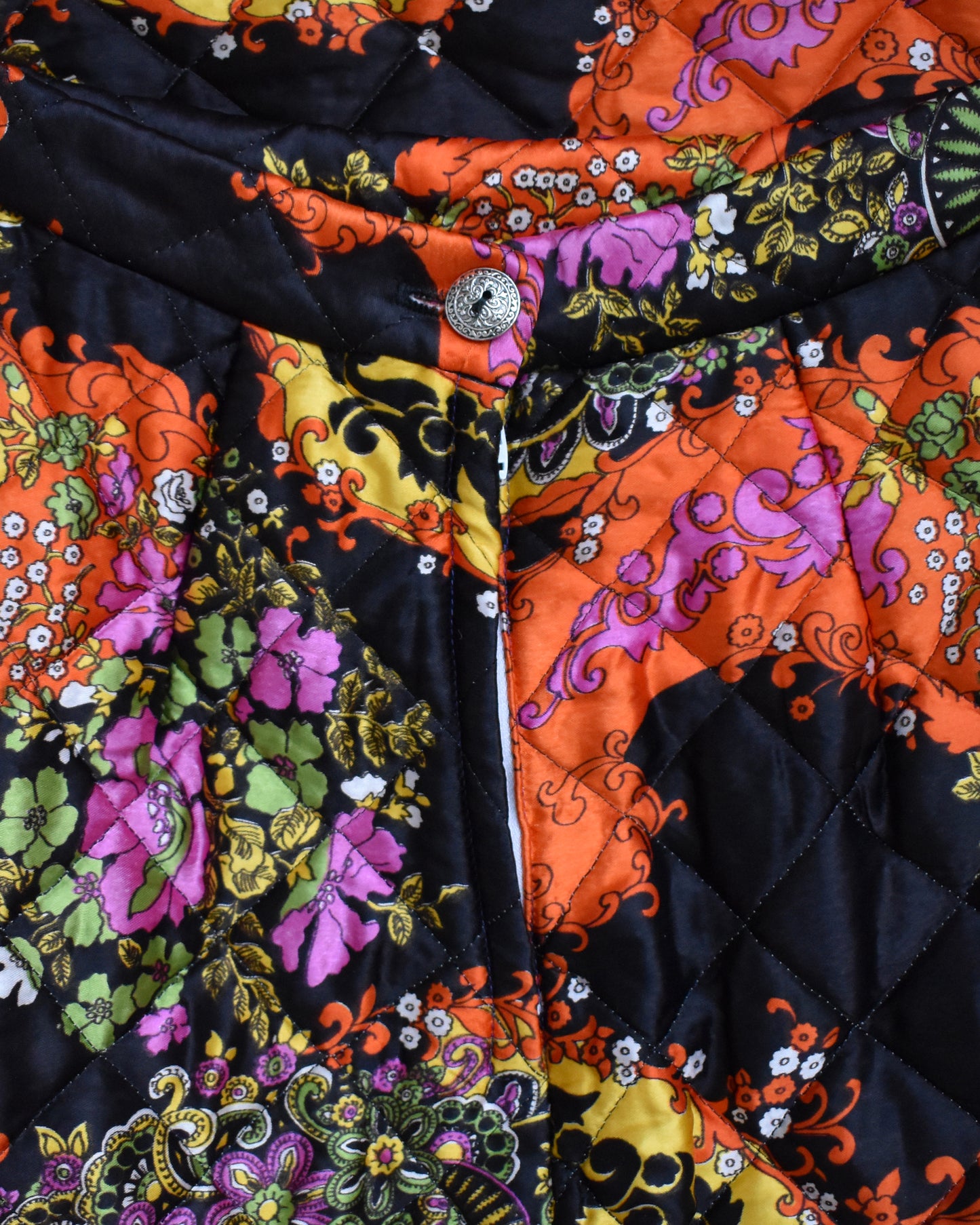 close up of the back button of a vintage 1970s black quilted skit that has a colorful floral and paisley print on a mannequin against a white background