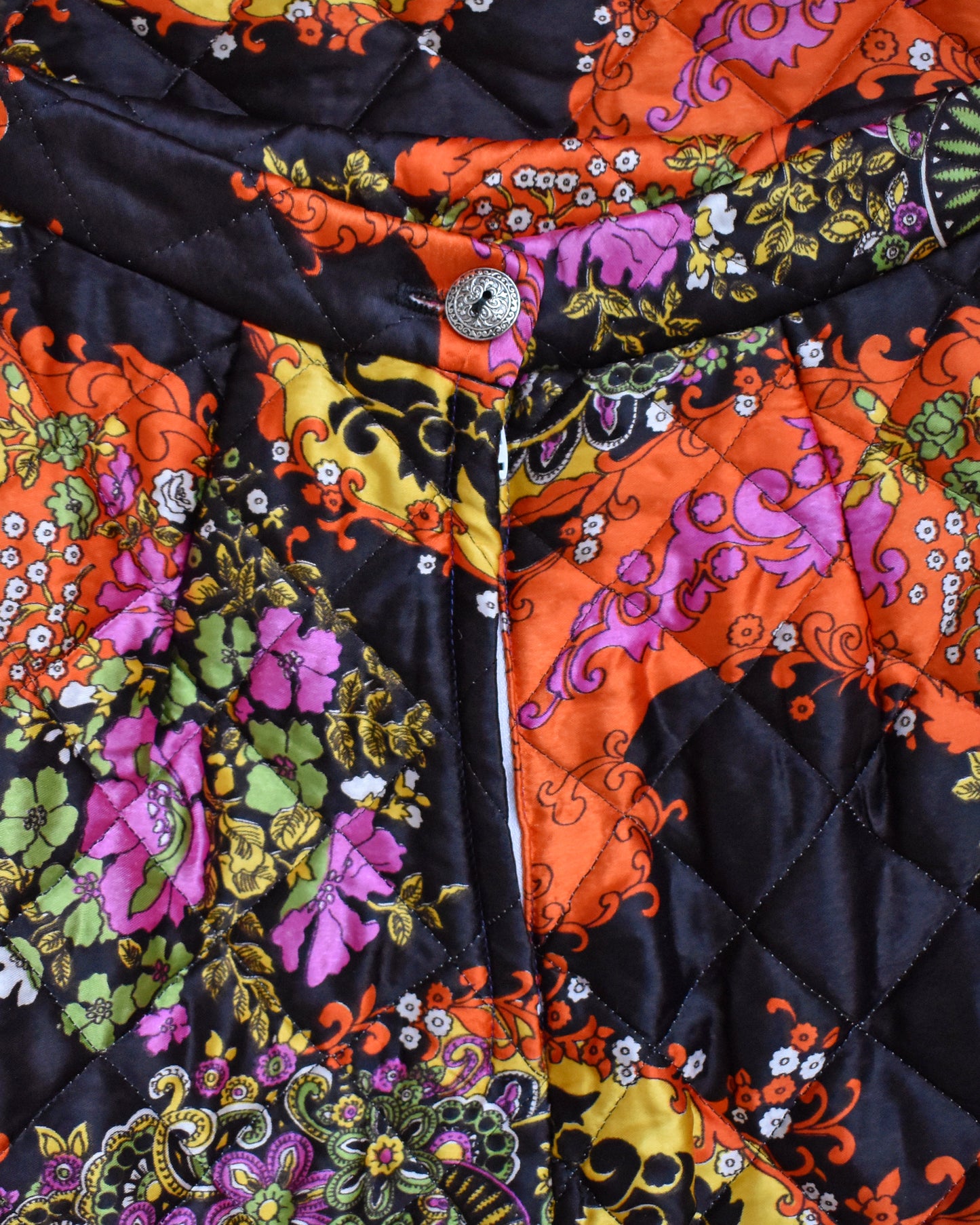 close up of the back button of a vintage 1970s black quilted skit that has a colorful floral and paisley print on a mannequin against a white background